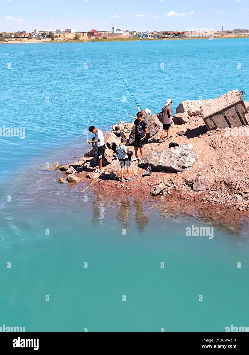 Balchash, Kasachstan - 16. August 2025: Mehrere junge Männer, die leidenschaftlich fischen, stehen am felsigen Ufer des Balchash-Sees. Die Fischer stehen auf Stockfoto
