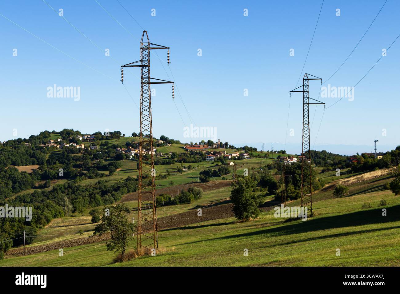 Ein ländliches italienisches Panorama mit zwei großen Hochspannungsmasten, die sich über eine grüne Landschaft erstrecken. Stockfoto