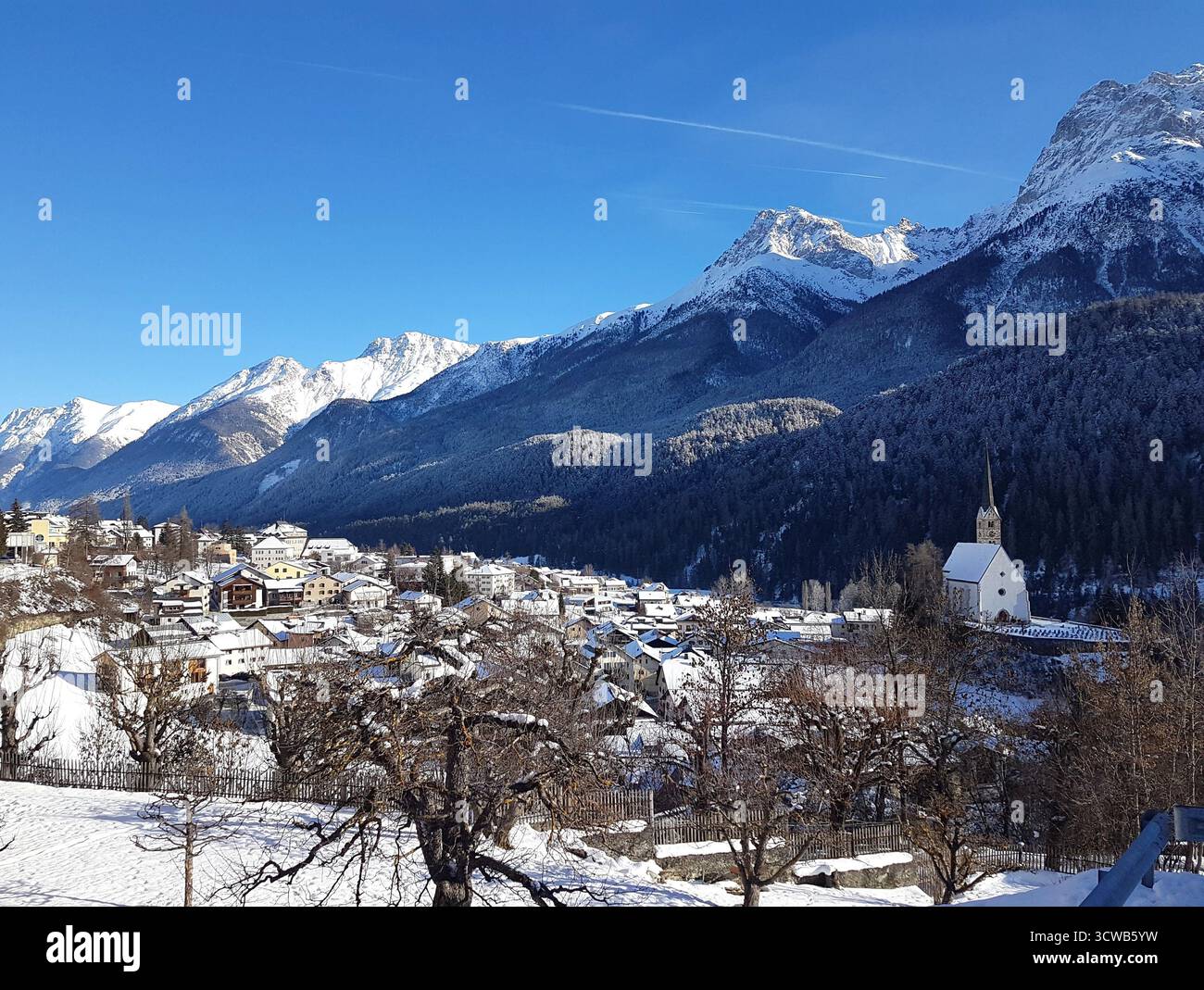 Ein atemberaubender Winterblick über das Engadintal mit dem Dorf Scuol umgeben von tiefem Schnee unter einem klaren blauen Himmel Stockfoto