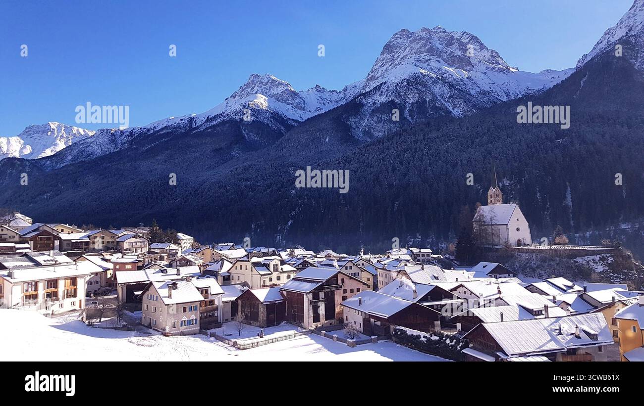 Ein atemberaubender Winterblick über das Engadintal mit dem Dorf Scuol umgeben von tiefem Schnee unter einem klaren blauen Himmel Stockfoto