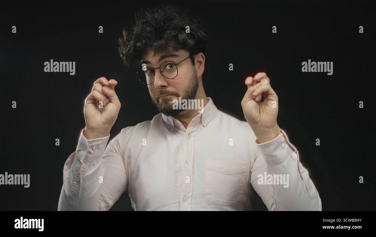Junger Mann mit Bart und Brille, der vor schwarzem Hintergrund eine Geste angibt, die Ausdruck und Geste in einem Studio zeigt. Stockfoto