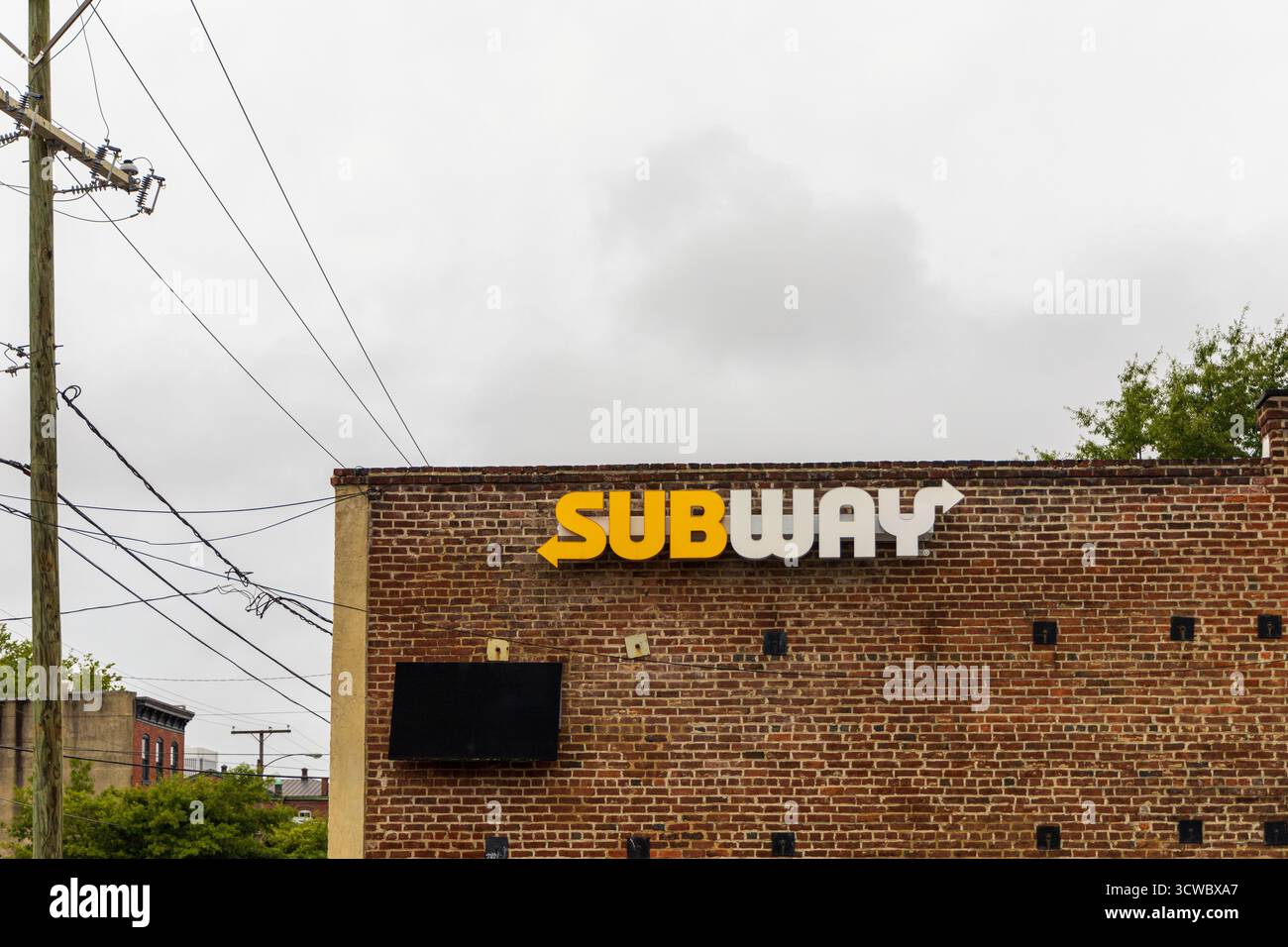 Ein Backsteingebäude mit einem U-Bahn-Schild drauf. Das Schild ist gelb und weiß. Der Himmel ist bewölkt. Richmond, Virginia. USA Stockfoto