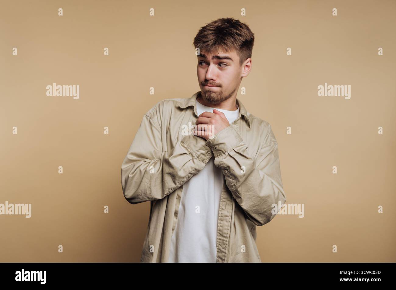 Porträt eines jungen Mannes mit kontemplativem Ausdruck hält seine Hände auf beigefarbenem Hintergrund zusammen Stockfoto