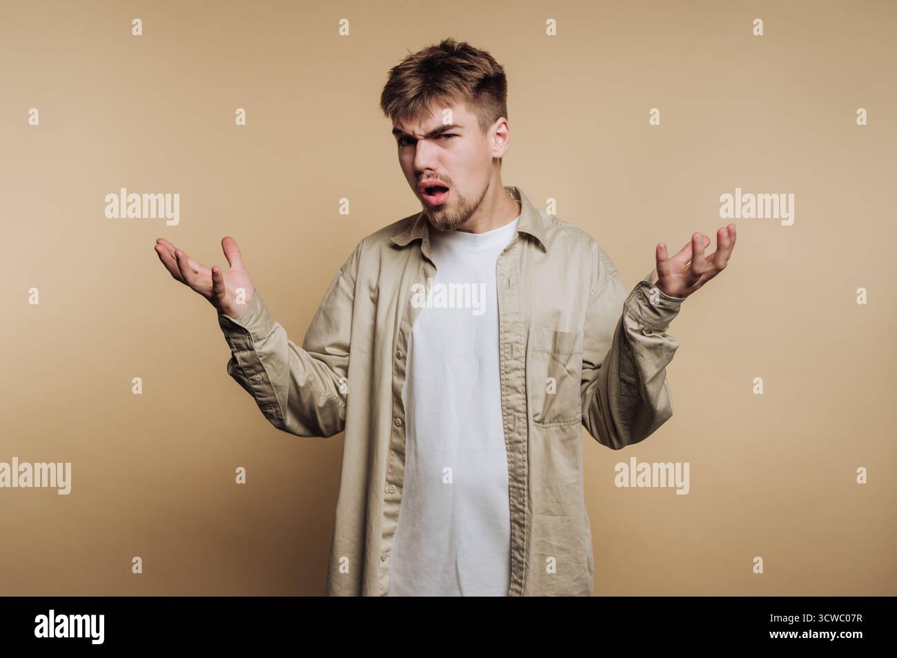 Das Porträt eines jungen frustrierten Mannes zeigt Verwirrung und Unglauben mit seinen Gesten auf beigefarbenem Hintergrund Stockfoto