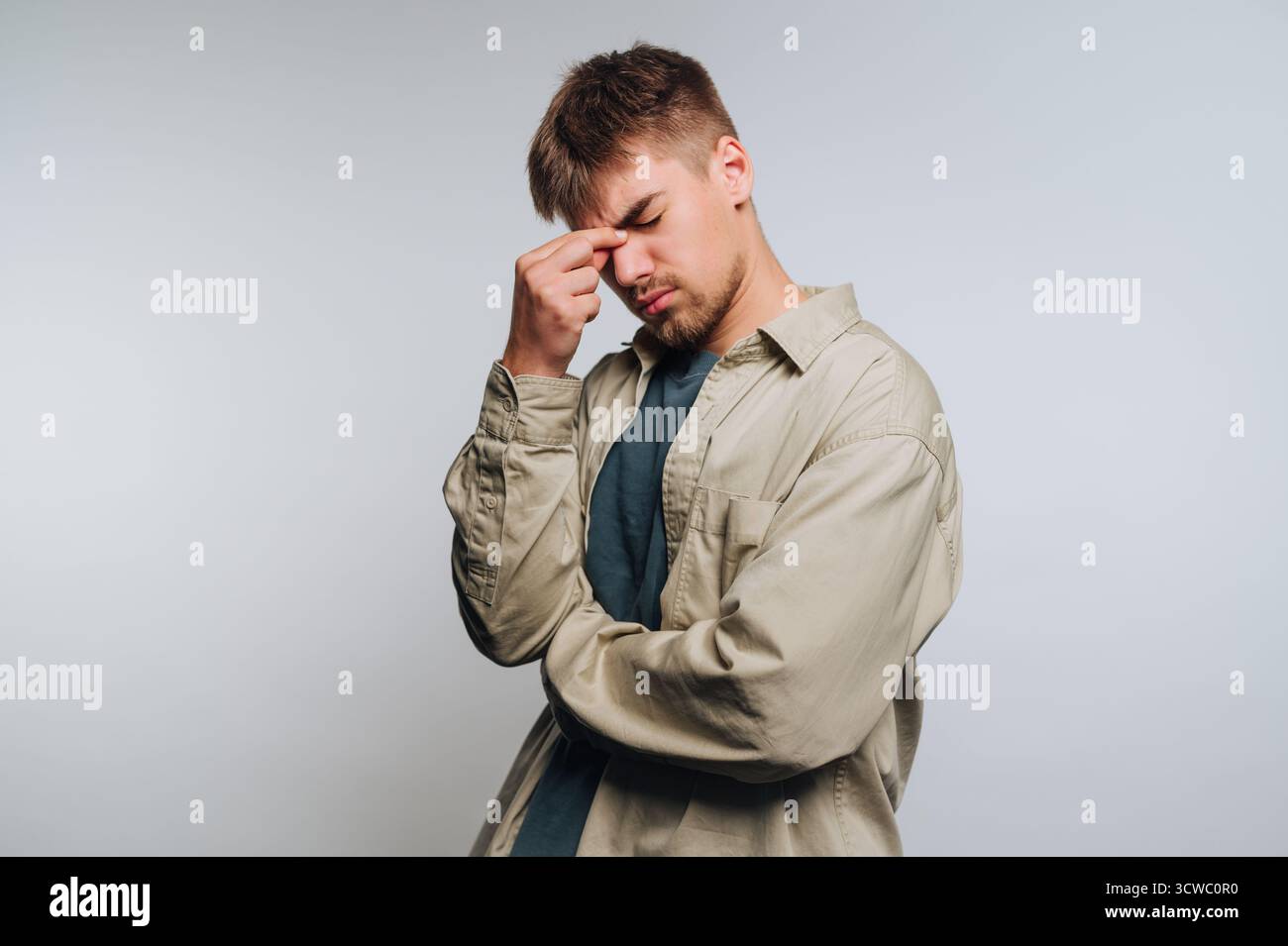 Porträt eines jungen Mannes drückt leichte Frustration aus, während er seine Stirn berührt und einen Moment der Besinnung auf weißem Hintergrund zeigt Stockfoto