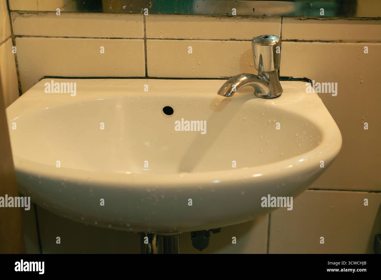 Weißes Keramikwaschbecken mit Chromarmatur, bedeckt mit Wassertropfen in Einem gefliesten Badezimmer Stockfoto