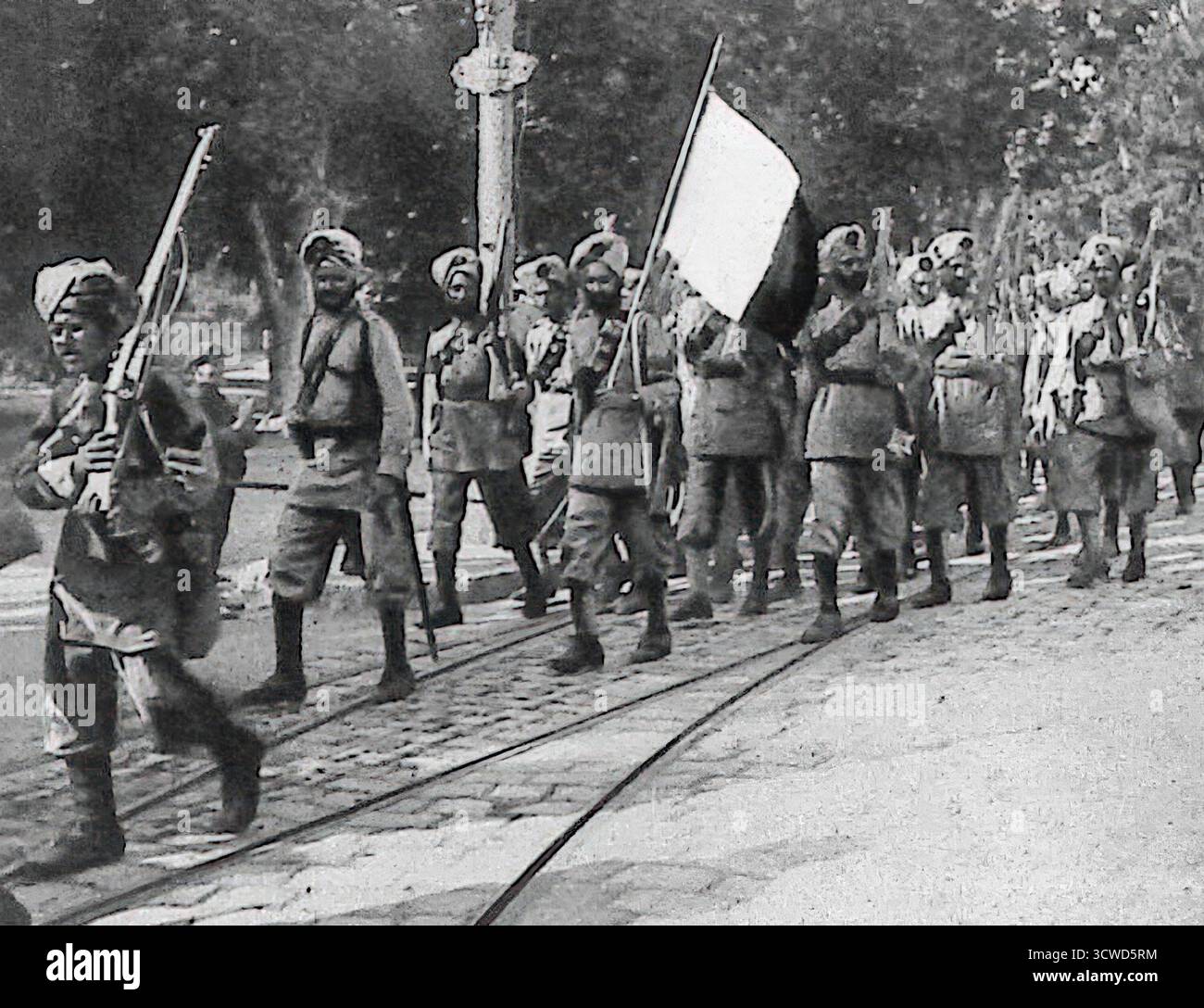 Ein Schwarzweiß-Bild aus Le Miroir vom Oktober 1914 zeigt Sikh-Soldaten, die in Marseille mit einer französischen Dreikolorenfahne marschieren. Diese symbolische Geste spiegelte die Solidarität zwischen Frankreich und den Kolonialeinheiten Indiens wider. Die Sikh-Regimenter, die Teil der British Indian Army waren, wurden zu einer sichtbaren Präsenz auf europäischem Boden, ihre Ankunft wurde in französischen Illustrationszeitschriften als Zeichen der Einheit der Alliierten im Ersten Weltkrieg gefeiert. Stockfoto