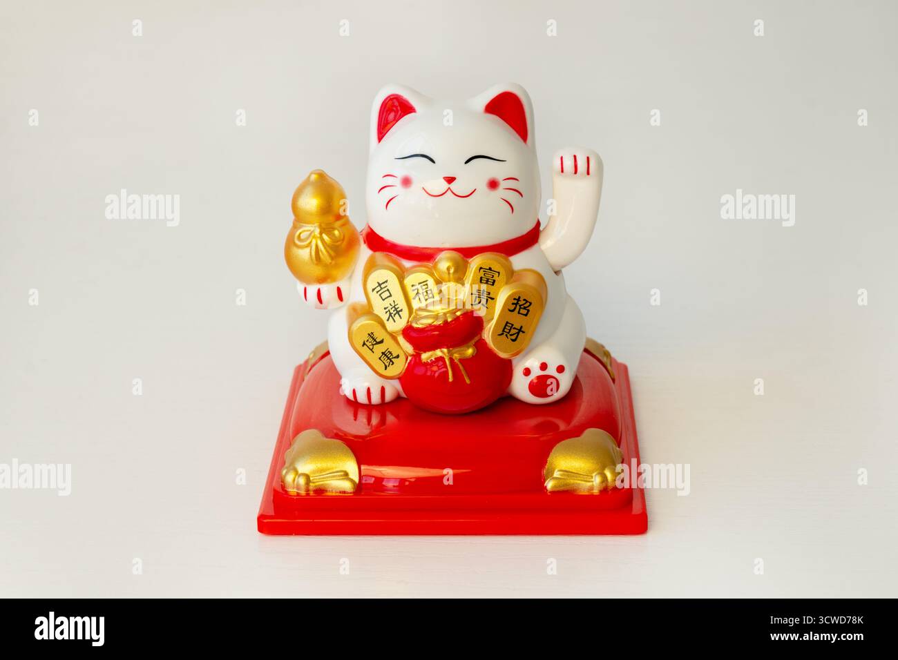 Maneki-neko. Japanische und chinesische Glückskatze auf weißem Hintergrund mit Kopierraum. Die Katze hält eine Münze, auf der gut geschrieben ist Stockfoto