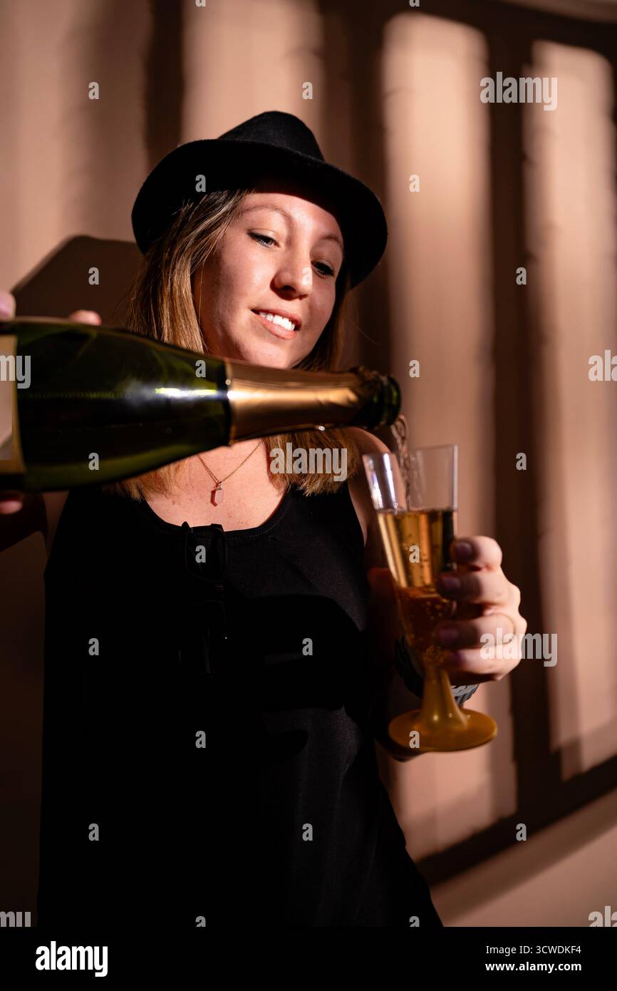 Eine junge Frau mit Hut feiert, Champagner in eine Flöte gießt Stockfoto
