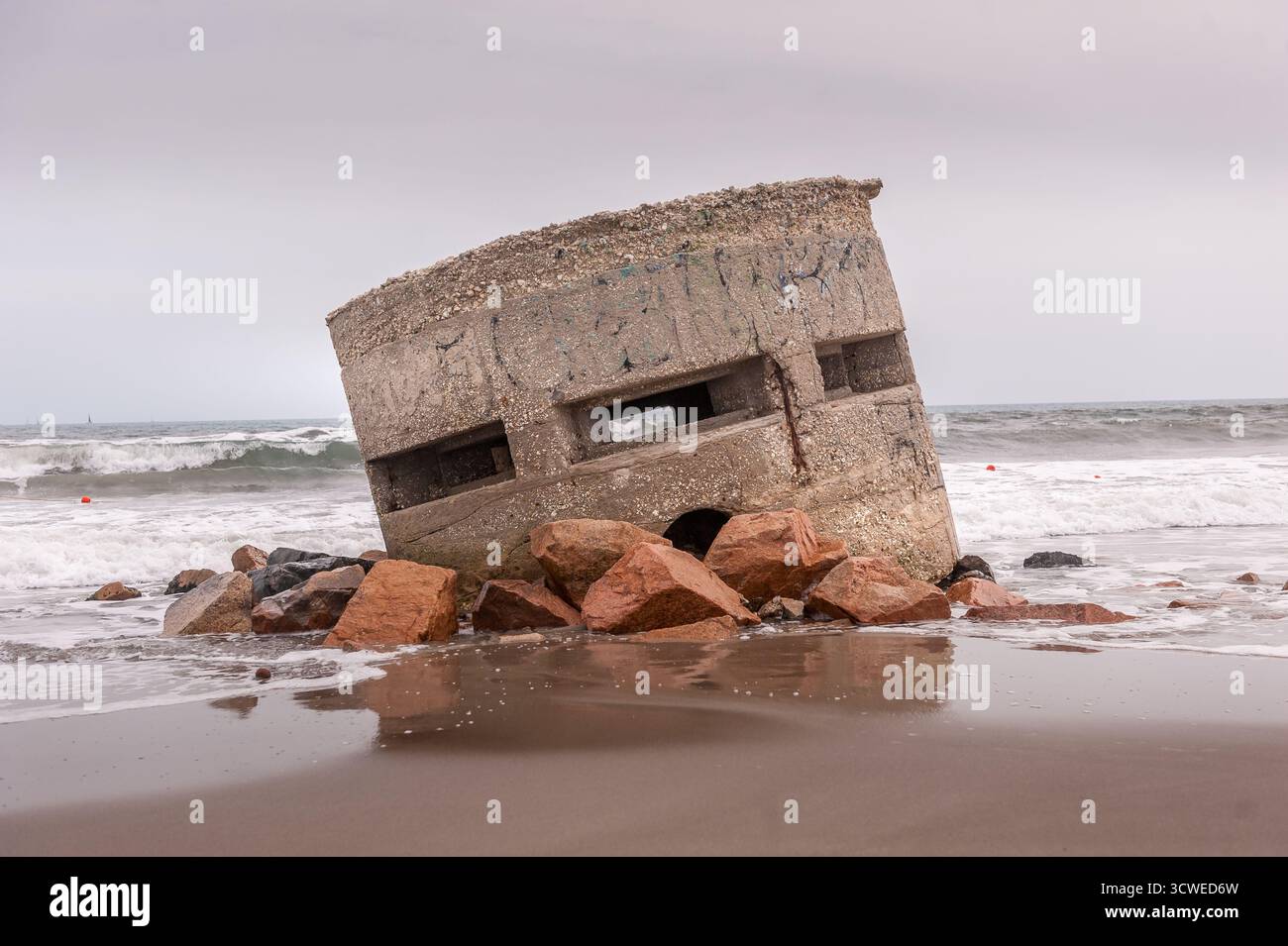 Der Bunker aus dem Zweiten Weltkrieg wurde teilweise am Poetto Beach, Cagliari, Sardinien, umrahmt von Felsen und Meereswellen. Stockfoto