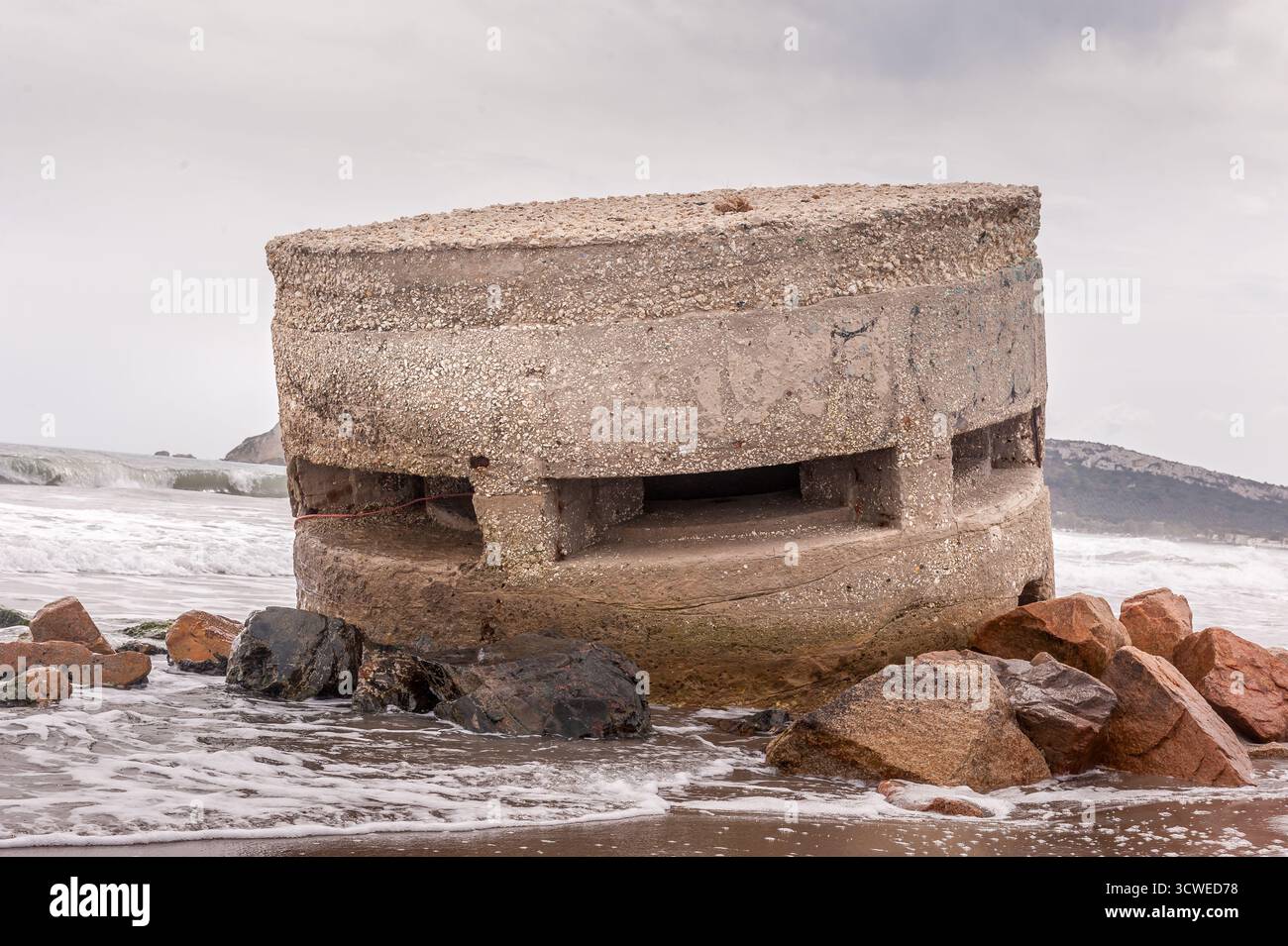 Der Bunker aus dem Zweiten Weltkrieg wurde teilweise am Poetto Beach, Cagliari, Sardinien, umrahmt von Felsen und Meereswellen. Stockfoto