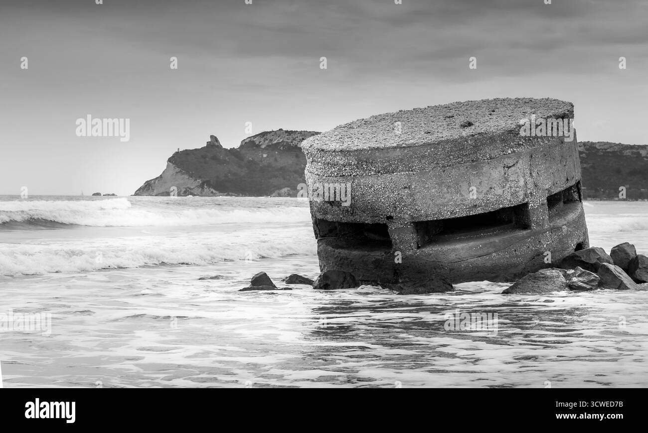 Der Bunker aus dem Zweiten Weltkrieg wurde teilweise am Poetto Beach, Cagliari, Sardinien, umrahmt von Felsen und Meereswellen. Stockfoto