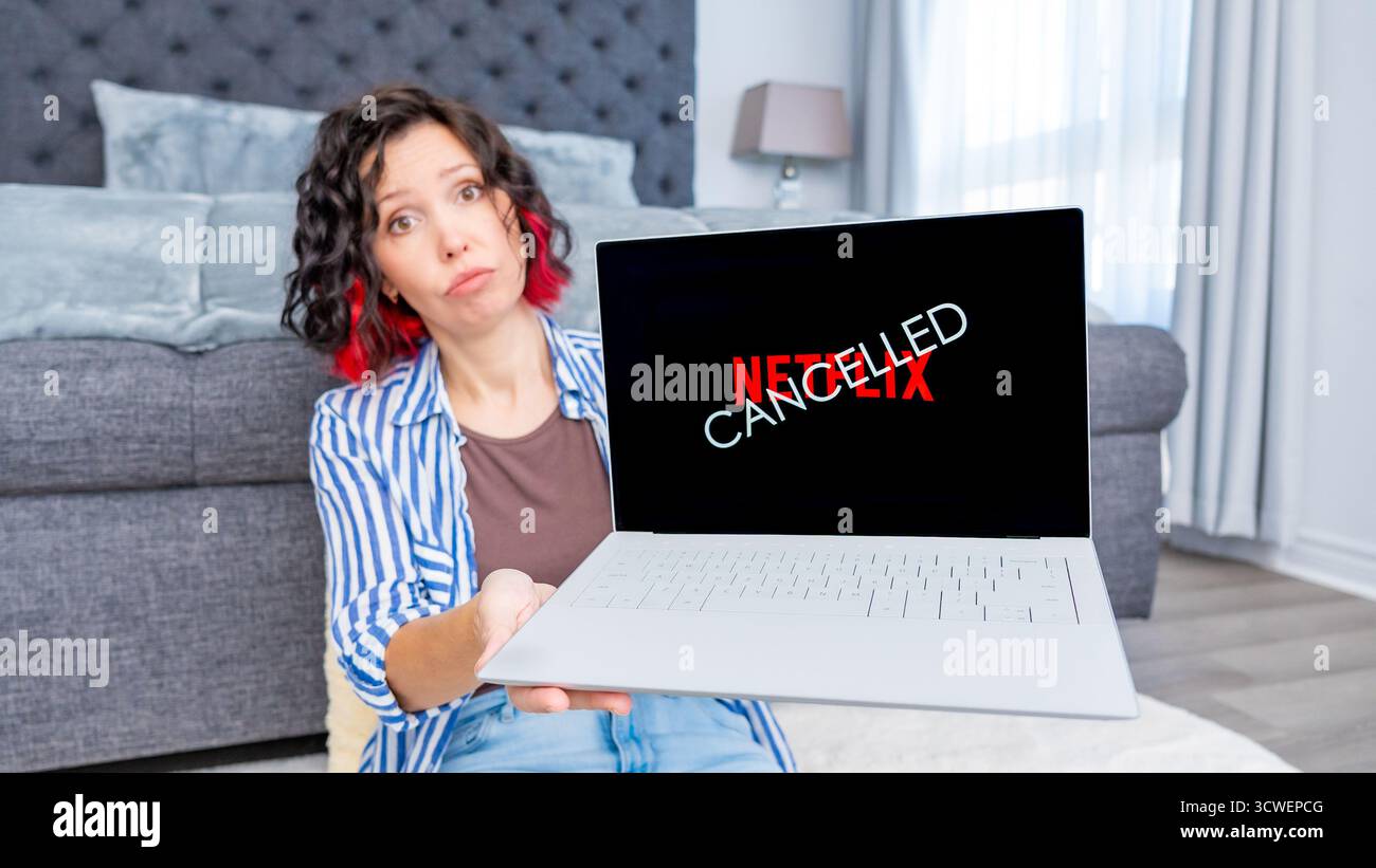 Ottawa ON, Kanada - 06. Oktober 2025: Frau mit lockigem Haar zeigt Laptop mit Netflix-Logo, sitzt auf dem Boden im Wohnzimmer und vermittelt ein Gefühl Stockfoto Ottawa ON, Kanada - 06. Oktober 2025: Frau mit lockigem Haar zeigt Laptop mit Netflix-Logo, sitzt auf dem Boden im Wohnzimmer und vermittelt ein Gefühl Stockfoto