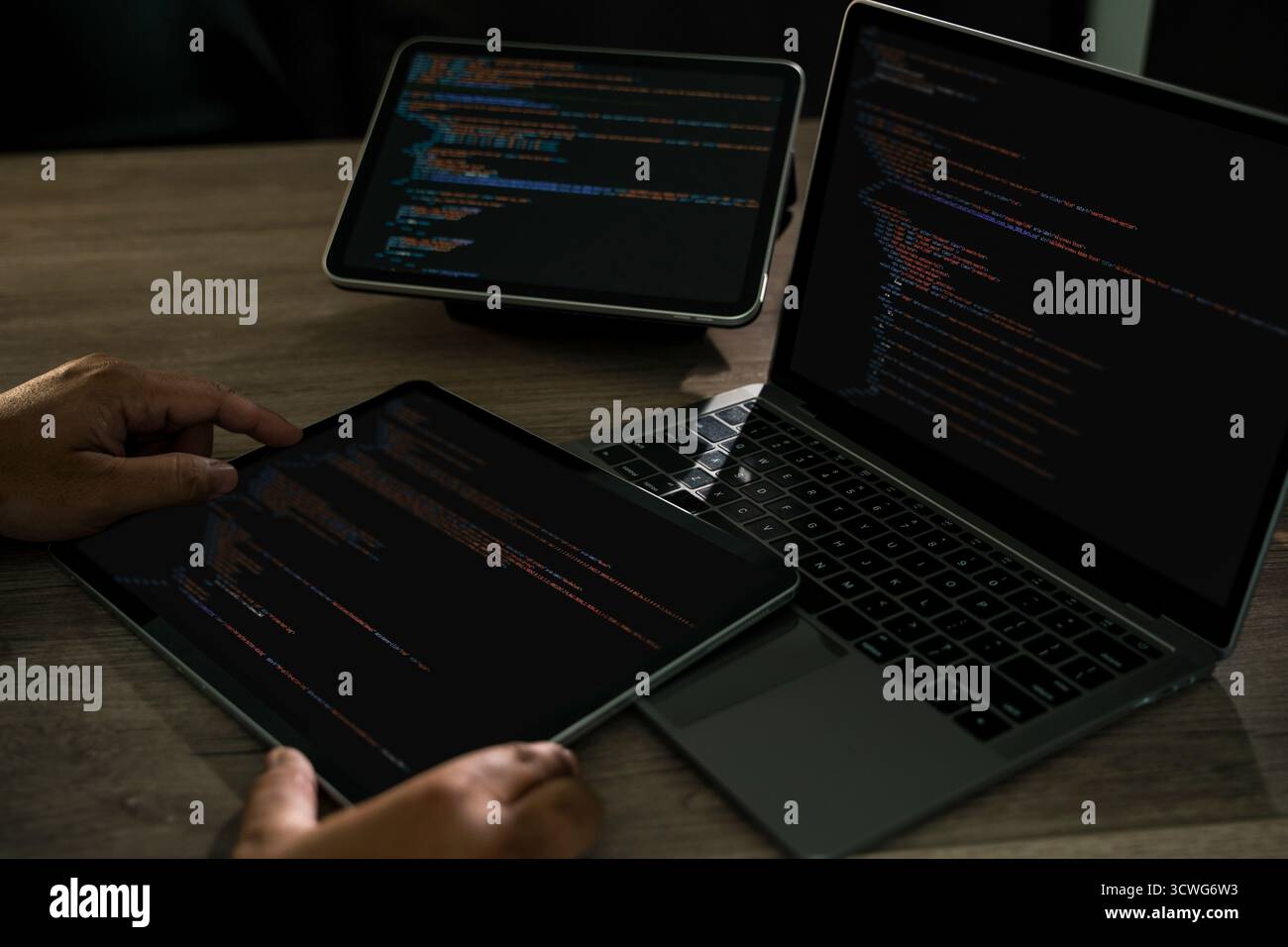 Programmierer schreibt Entwicklungswebsite-Design-Code an einem Schreibtisch mit Laptop und Tablet, dunklem Arbeitsbereich, Handtastatur, css und HTML moderner Software de Stockfoto