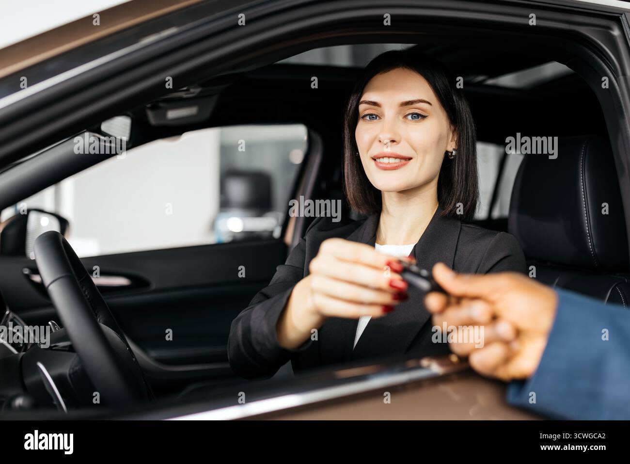Eine professionelle Frau in einem schwarzen Anzug erhält die Schlüssel von einem Verkäufer in einem eleganten Ausstellungsraum, in dem der Kaufprozess und c hervorgehoben werden Stockfoto