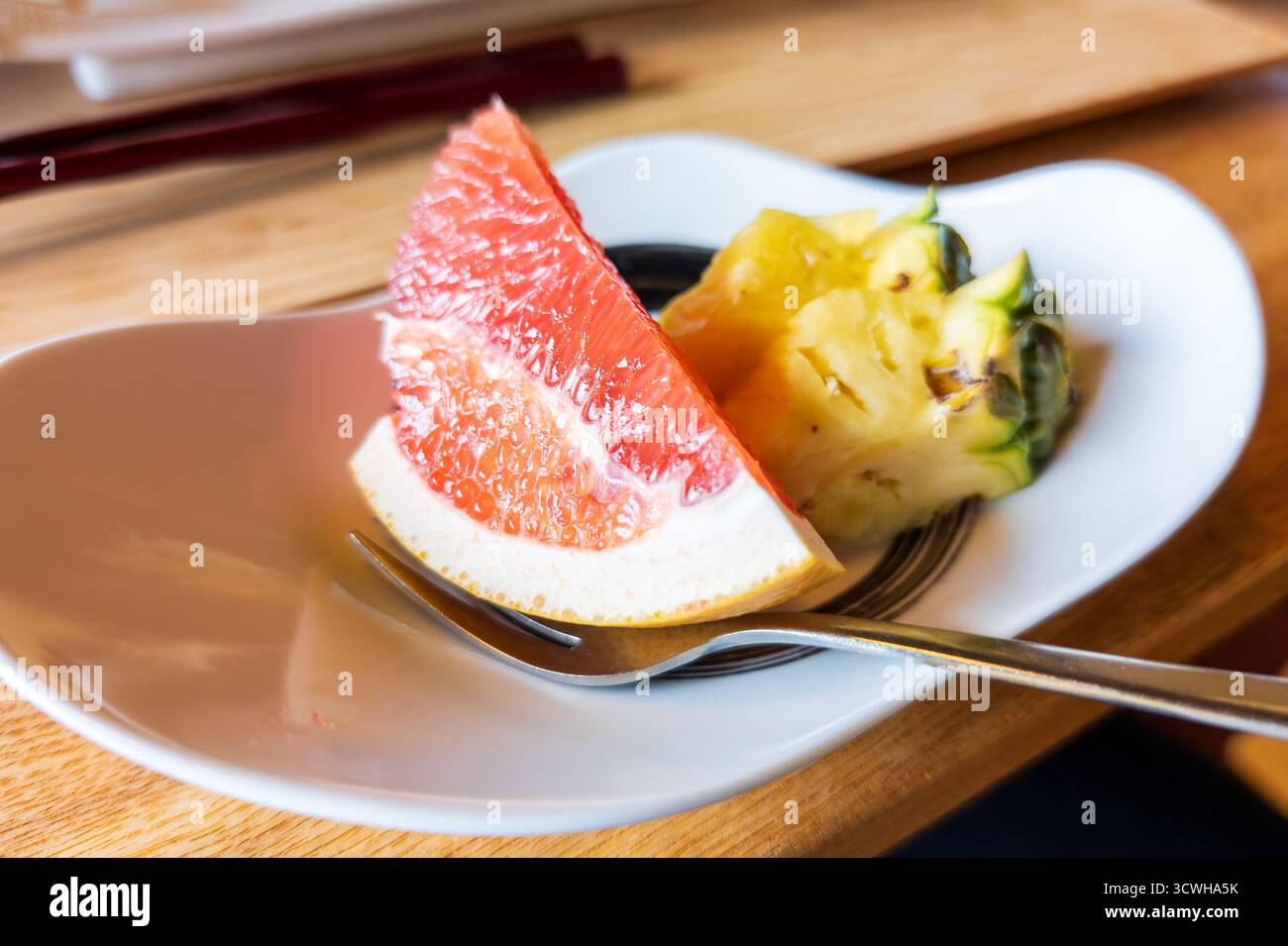 Scheiben frischer roter Grapefruit und saftiger Ananas auf einem modernen weißen Dessertteller Stockfoto