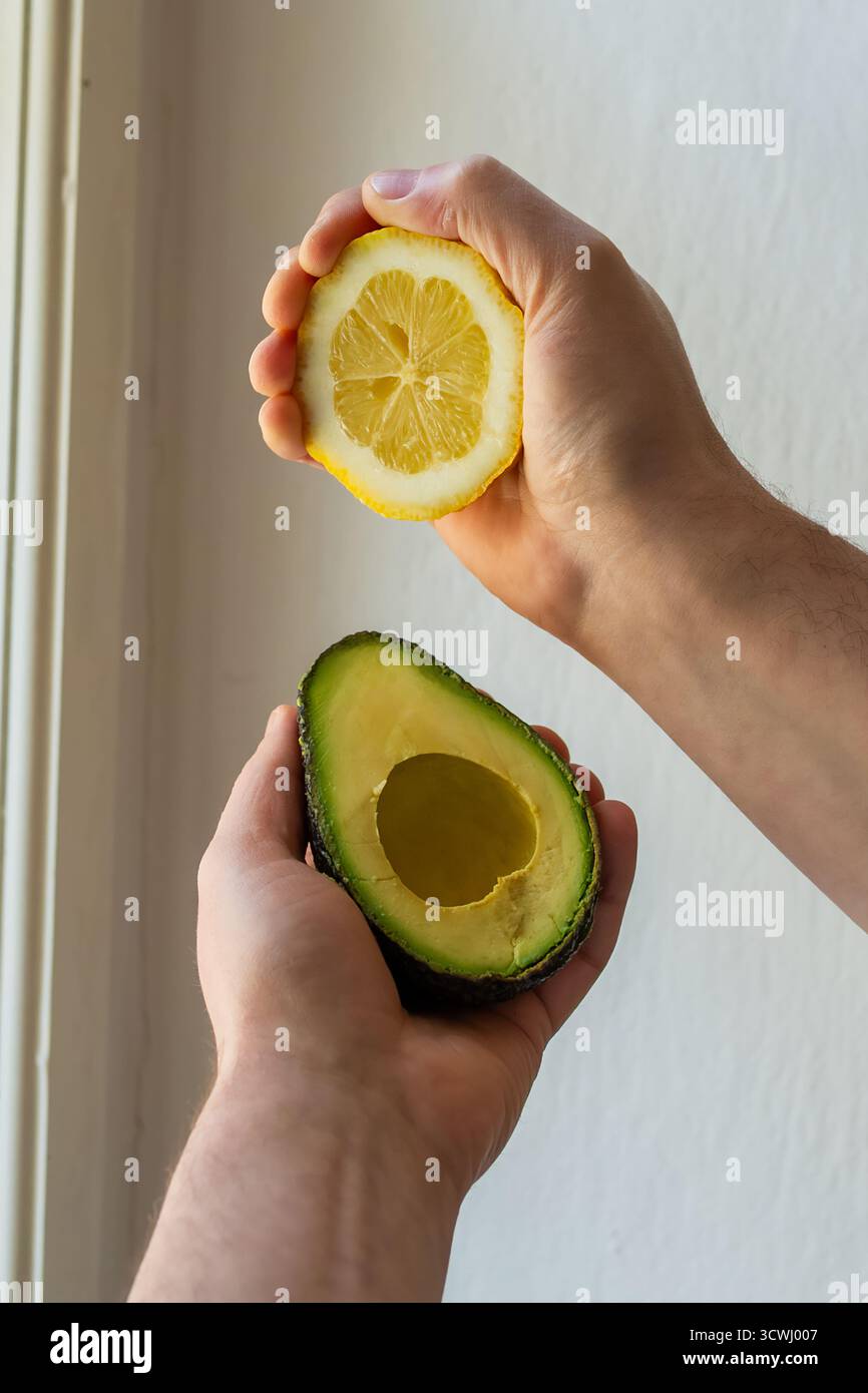 In Scheiben geschnittene Avocado und Zitrone in den Händen gehalten. Rohkost (Obst und Gemüse), beleuchtet durch natürliches Licht. Frische Zutaten für das Guacamole-Rezept. Gesund Stockfoto