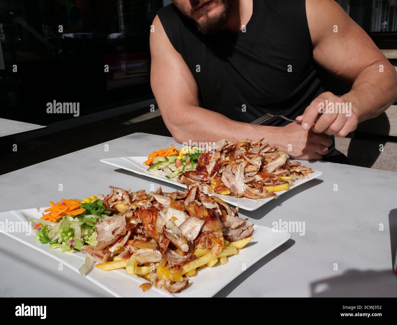 Zwei Teller gegrilltes Shawarma/Gyros-Fleisch mit Pommes Frites und Salat auf einem weißen Tisch im Freien, während eine Person mit einem Fo beginnt Stockfoto