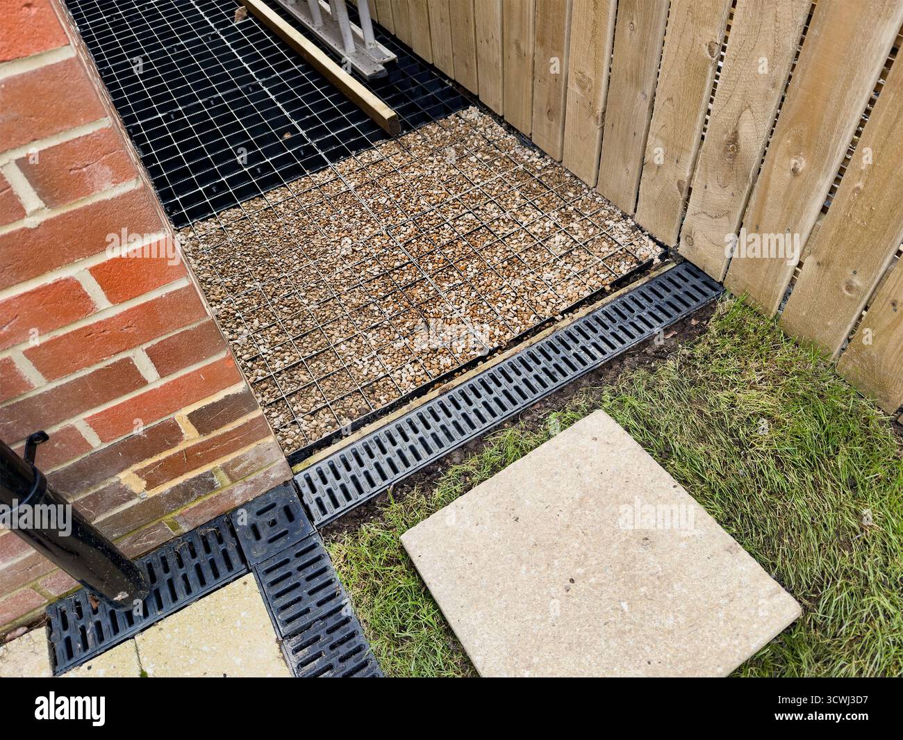 Abflusslösung für den Außenbereich mit Gitterabdeckung und Steinziegel in der Nähe von Ziegel- und Holzzaun im Gartenbereich - Smartphone-aufgenommenes Stockfoto