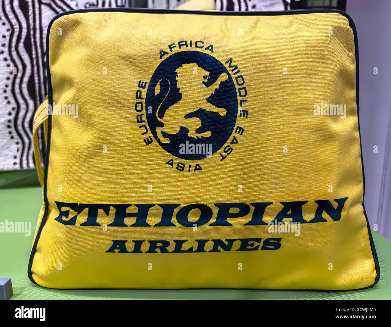 Gelbe Handgepäcktasche von Ethiopian Airlines mit dem Emblem der Fluggesellschaft mit einem Löwen und Kontinenten auf grüner Oberfläche - Smartphone-aufgenommenes Stockfoto