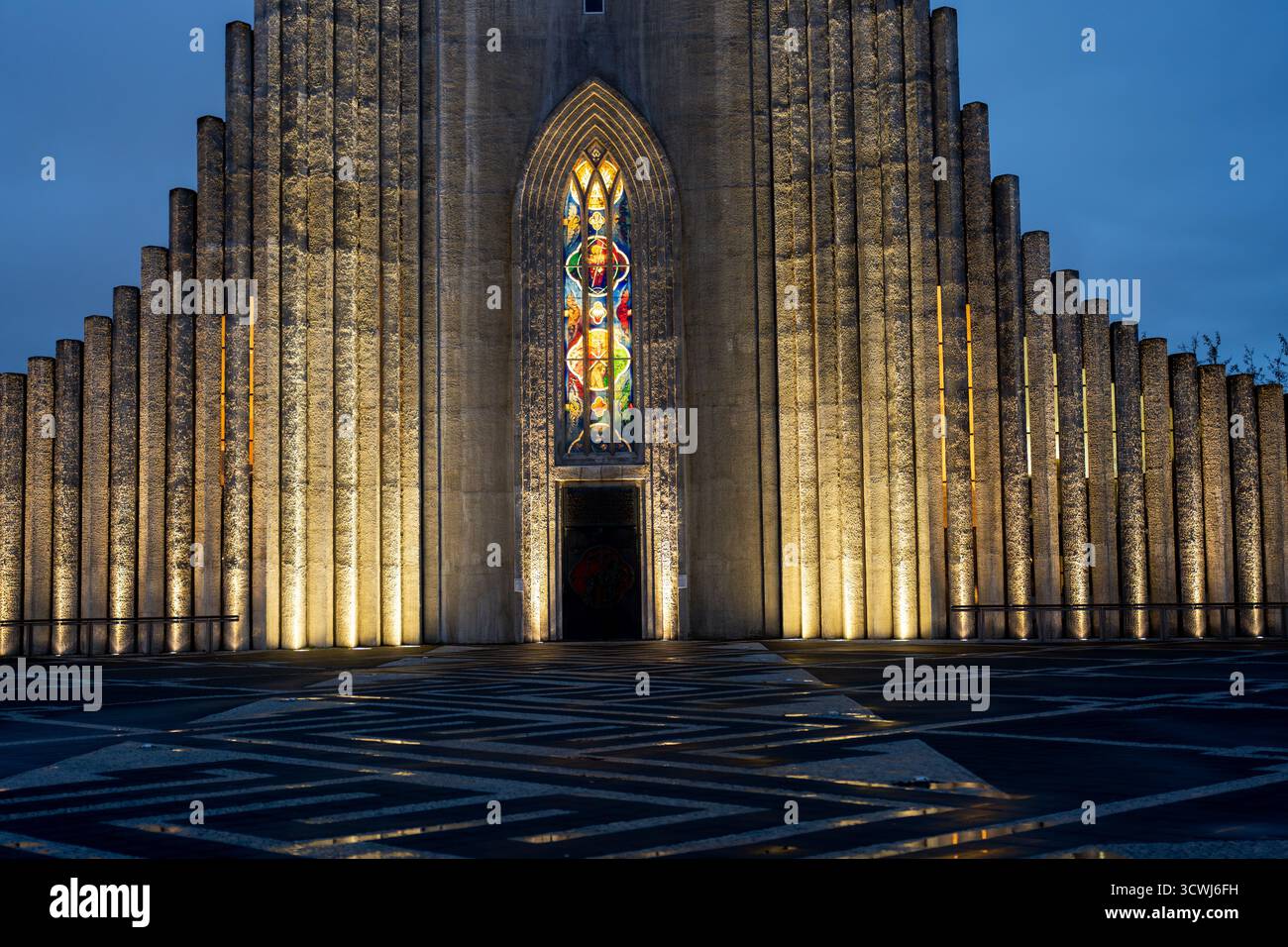 Hallgrimskirkjas beleuchtete Fassade mit Basaltsäulen, bogenförmigem Eingang, Buntglasfenster und geometrischen Mustern in Reykjavik, Island. Stockfoto