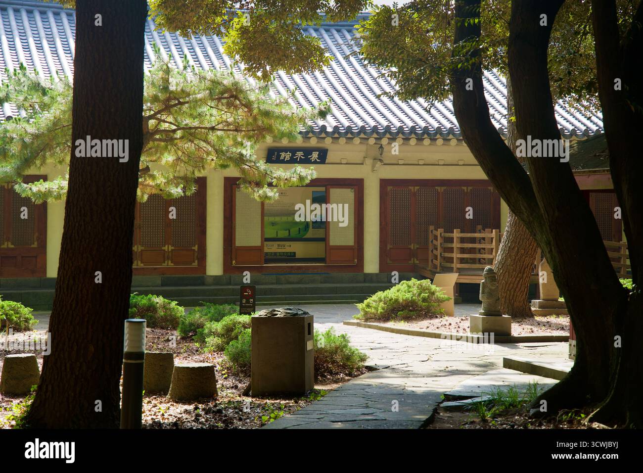 Blick durch Bäume zum Samseonghyeol Museumsgebäude mit Schautafeln und Holztüren, mit Sträuchern und Steinpfaden. Stockfoto