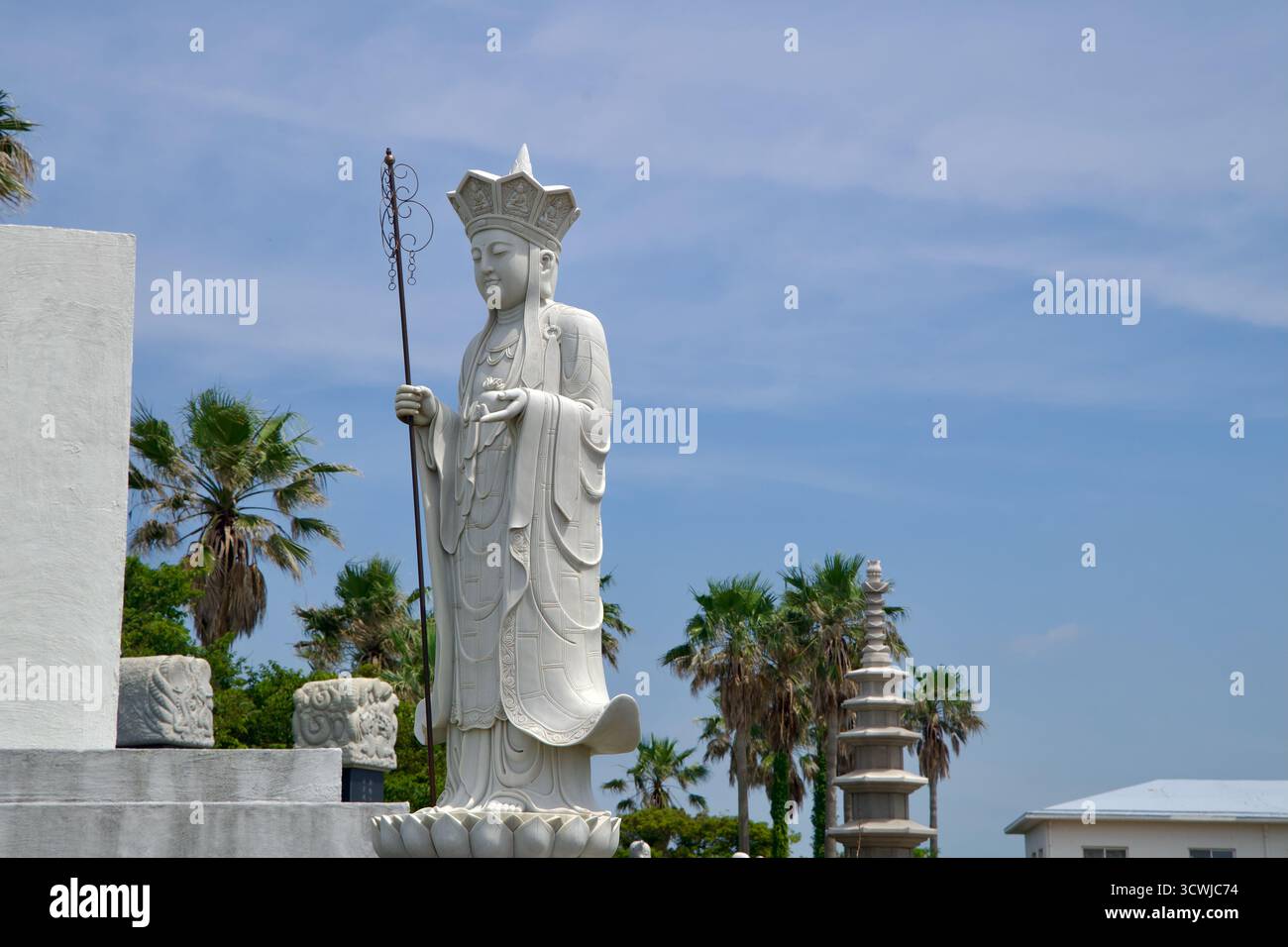 Aus nächster Nähe sehen Sie eine stehende Bodhisattva-Statue, die einen Mitarbeiter im Buddha Sharira Stupa-Komplex hält, mit einer mehrstöckigen Steinpagode und Palmen, die sich erheben Stockfoto