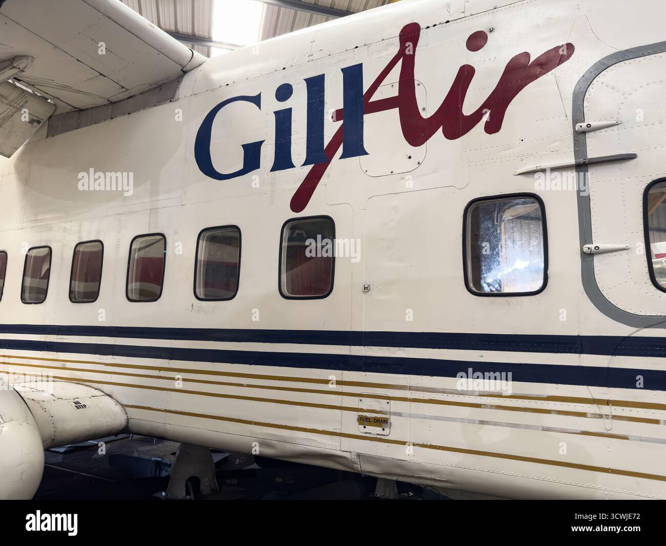 Seitenansicht eines Gill Air-Flugzeugs, das in einem Hangar mit sichtbarem Branding und mehreren Fenstern unter sanfter Beleuchtung in newcastle geparkt ist - Smartphone-aufgenommenes Stockfoto