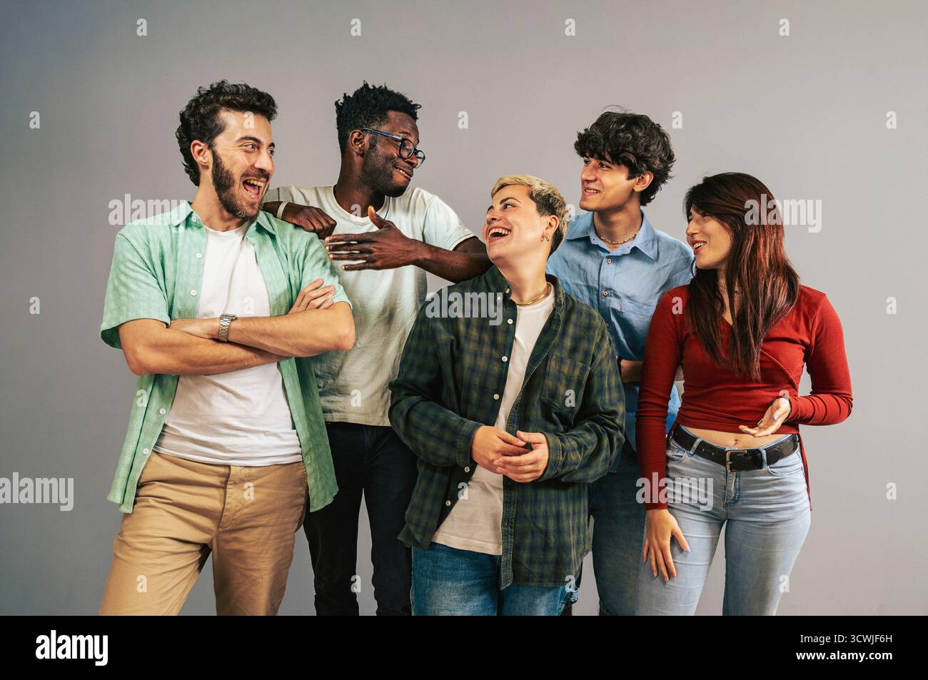 Eine fröhliche, multiethnische Gruppe von fünf jungen Freunden in lässiger Kleidung, die lachen und eine positive Interaktion miteinander haben, während sie in einem Studio stehen Stockfoto