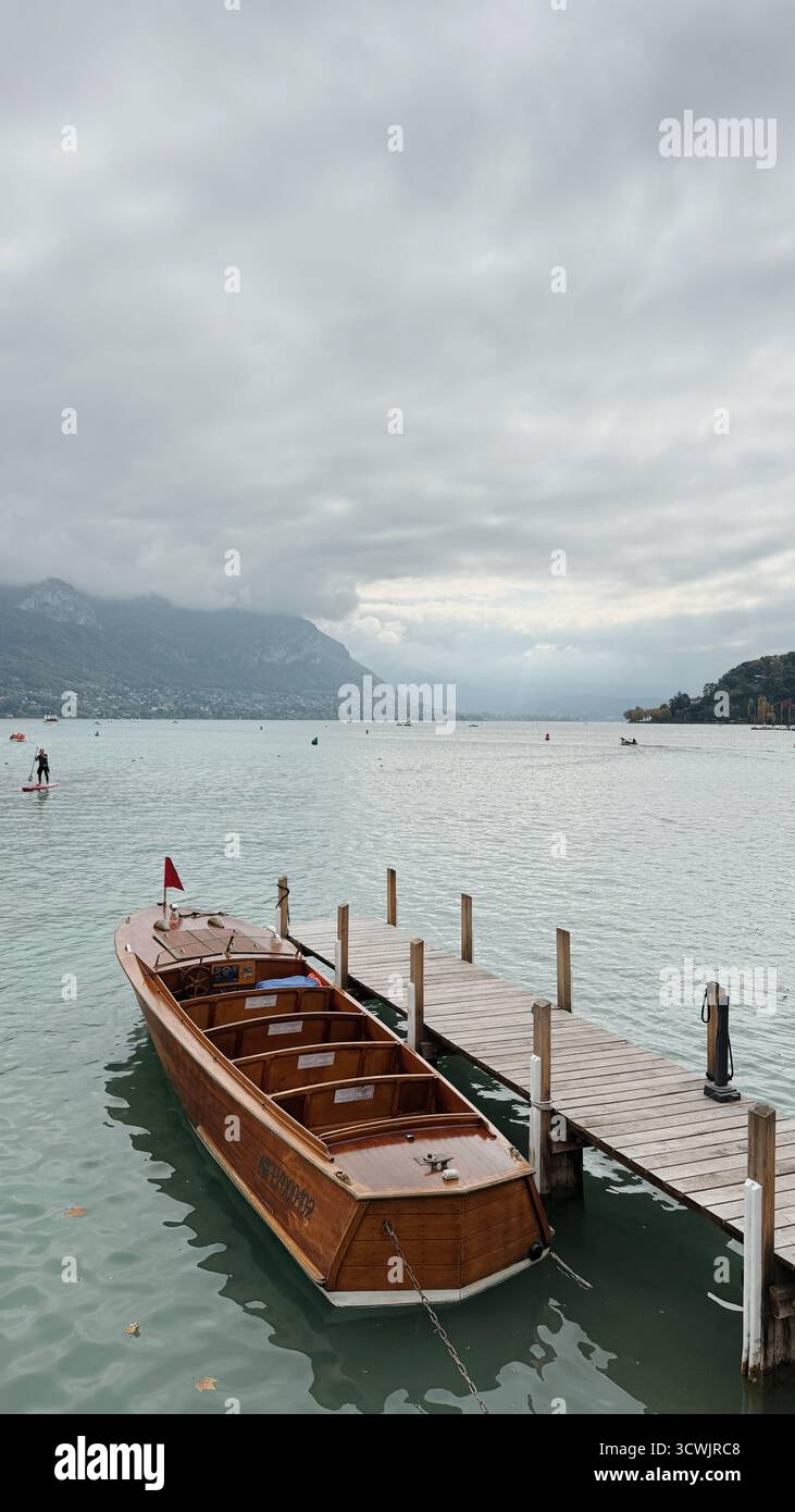 Holzboot, das am See Annecy mit Bergen und Wolken in Haute-Savoie, Frankreich, ankert - Smartphone-aufgenommenes Stockfoto