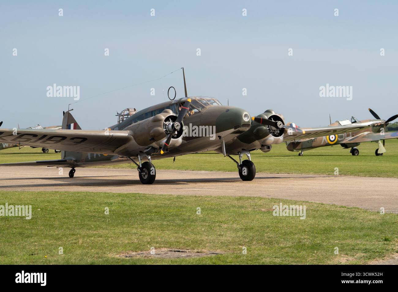 Historische zweimotorige RAF-Flugzeuge, die auf der Start- und Landebahn auf dem Duxford-Flugplatz mit Spitfire im Hintergrund unterwegs sind Stockfoto