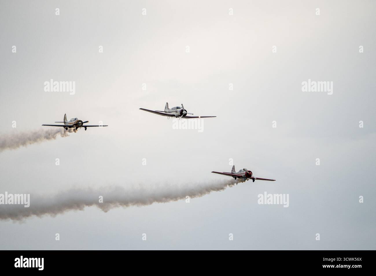 Drei Oldtimer-Flugzeuge mit Kunstflugzeugen und Rauchspuren vor grauem Himmel Stockfoto