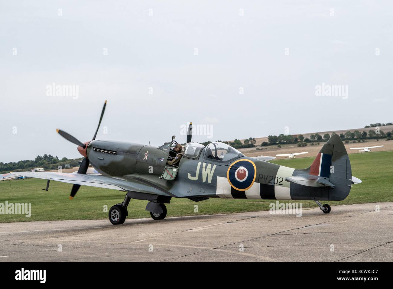 RAF Spitfire Kampfflugzeuge auf der Landebahn auf dem Duxford Flugplatz mit sichtbarem Piloten im Cockpit Stockfoto