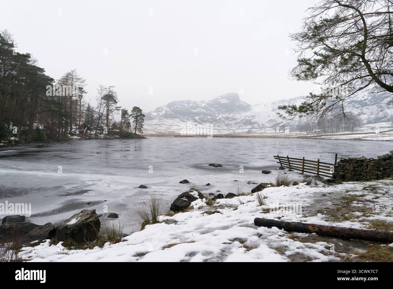 Gefrorenes Blea Tarn mit schneebedeckten Fjällen und Holzzaun in der winterlichen Landschaft des Lake District Stockfoto