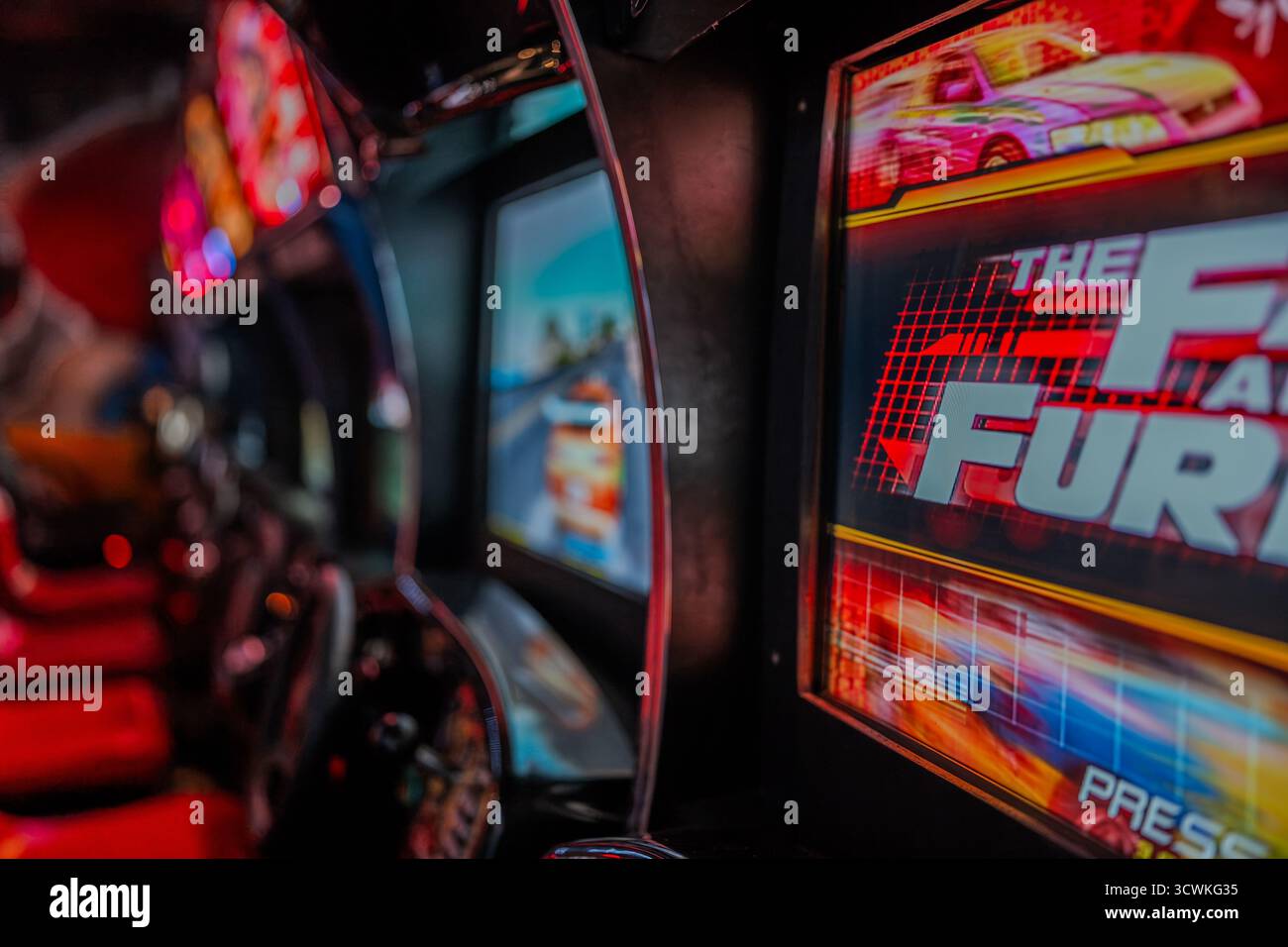 Eine Nahaufnahme des Spielkabinetts der Spielhalle Fast and the Furious Arcade mit leuchtenden Bildschirmen und einem Lenkrad in einer Retro-Arcade Stockfoto