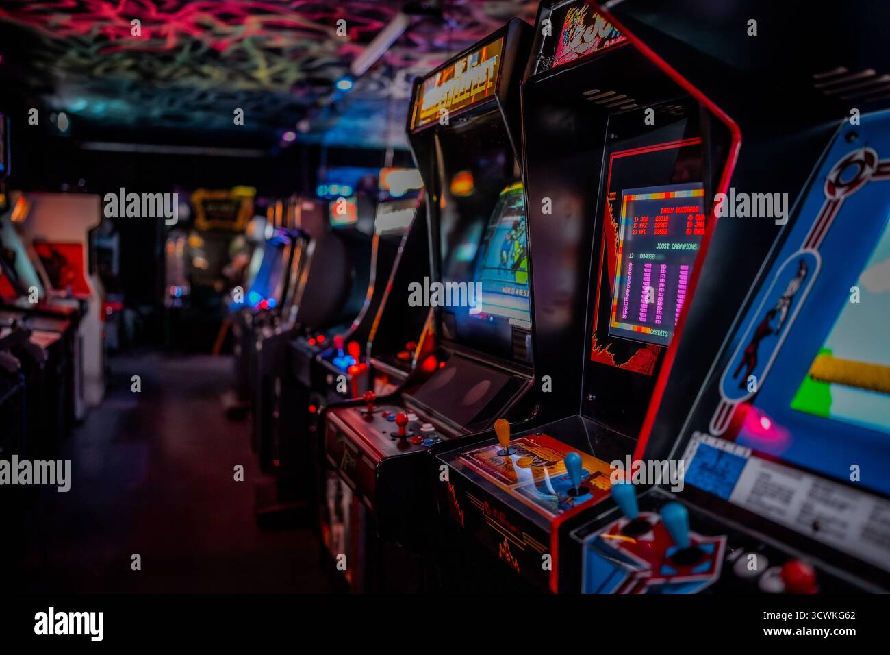 Klassische Spielautomaten mit leuchtenden Bildschirmen sind in einem Retro-Spielezentrum angeordnet Stockfoto