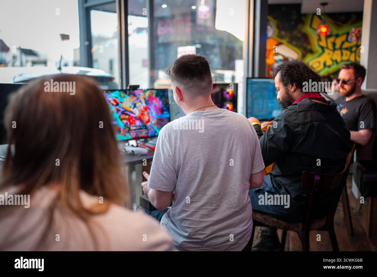 Gamer spielen kämpfende Videospiele auf Monitoren während eines Arcade-Events mit Graffiti-Grafiken im Hintergrund Stockfoto
