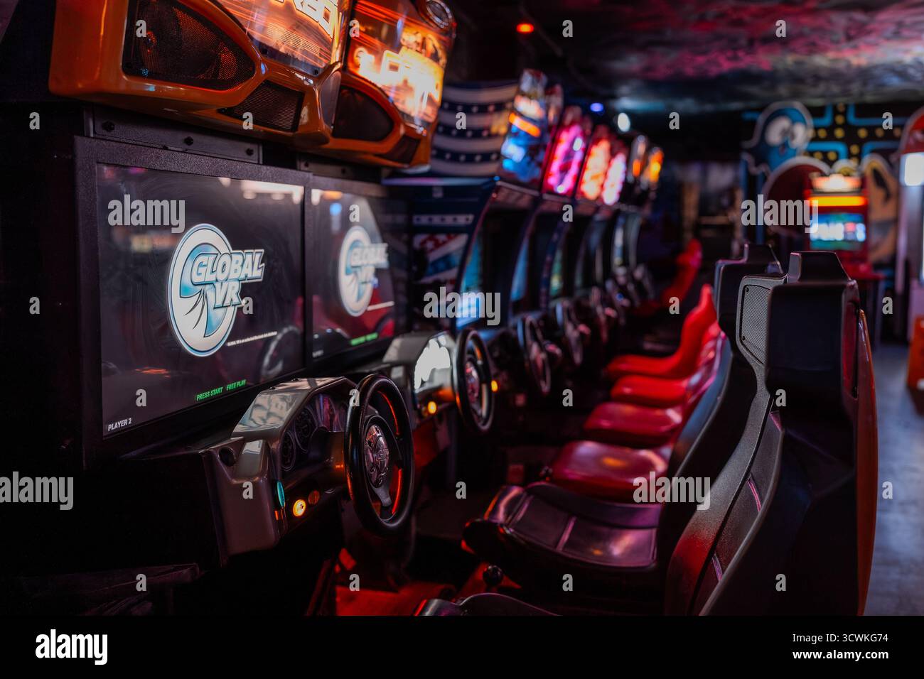Eine Reihe von Global VR-Automaten mit glühenden Lenkrädern und Neonlichtern Stockfoto