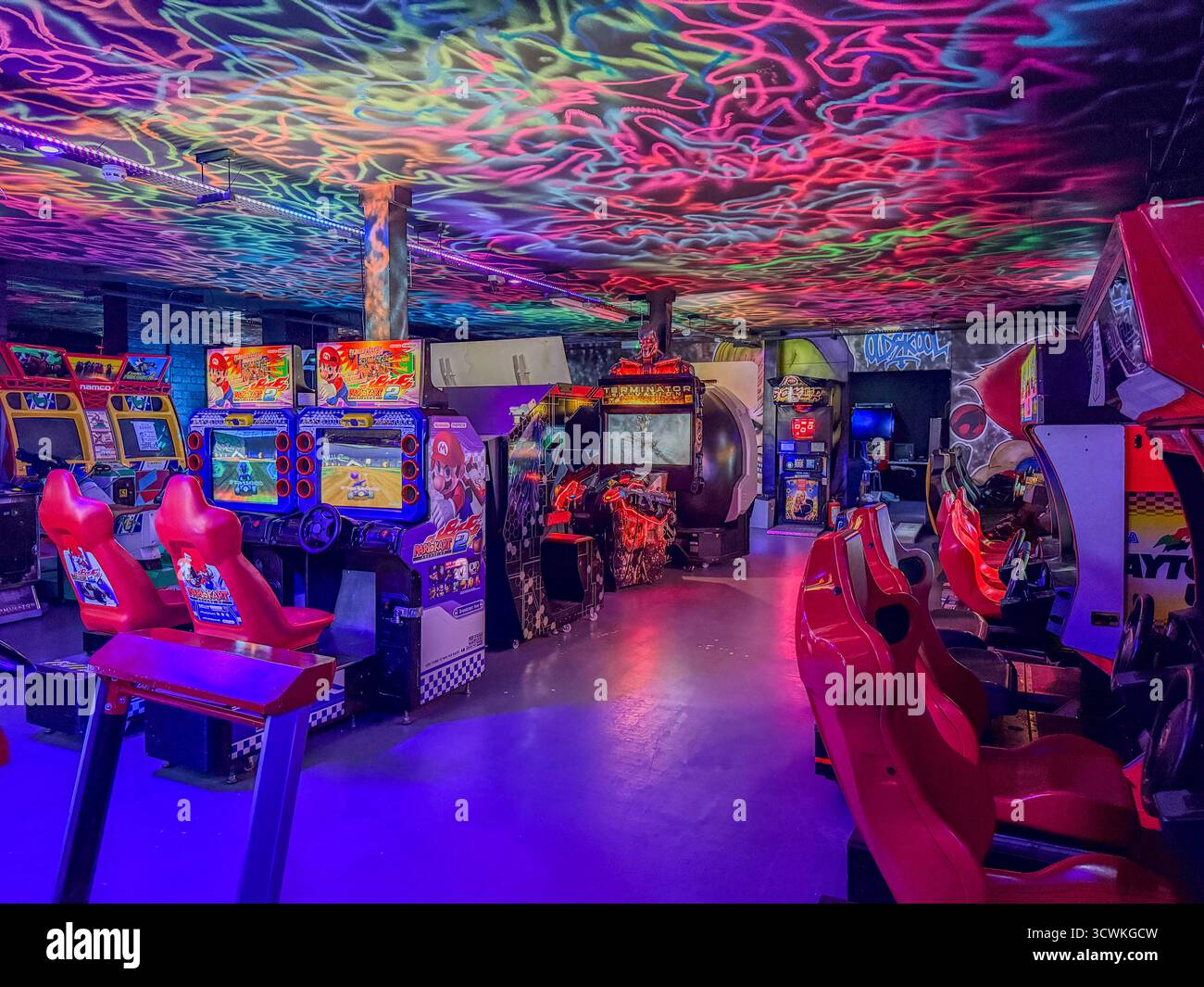 Das neonbeleuchtete Interieur einer Retro-Arkade mit Mario Kart GP2, Terminator Salvation und Daytona USA Maschinen Stockfoto