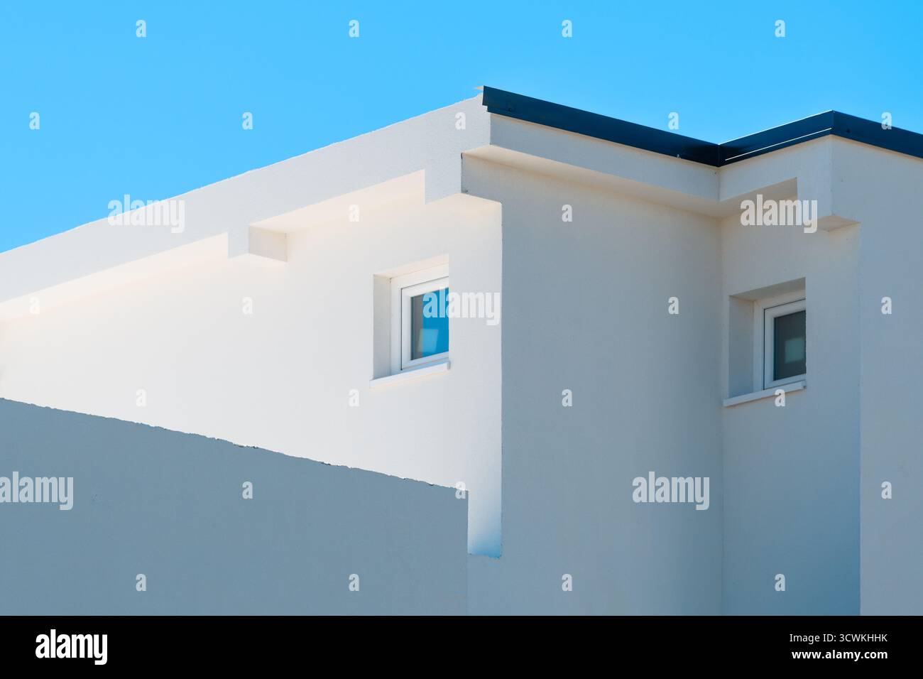 Modernes weißes minimalistisches Gebäude mit geometrischen Linien und Fenstern unter klarem blauem Himmel, zeitgenössische mediterrane Architektur. Selektiver Fokus Stockfoto