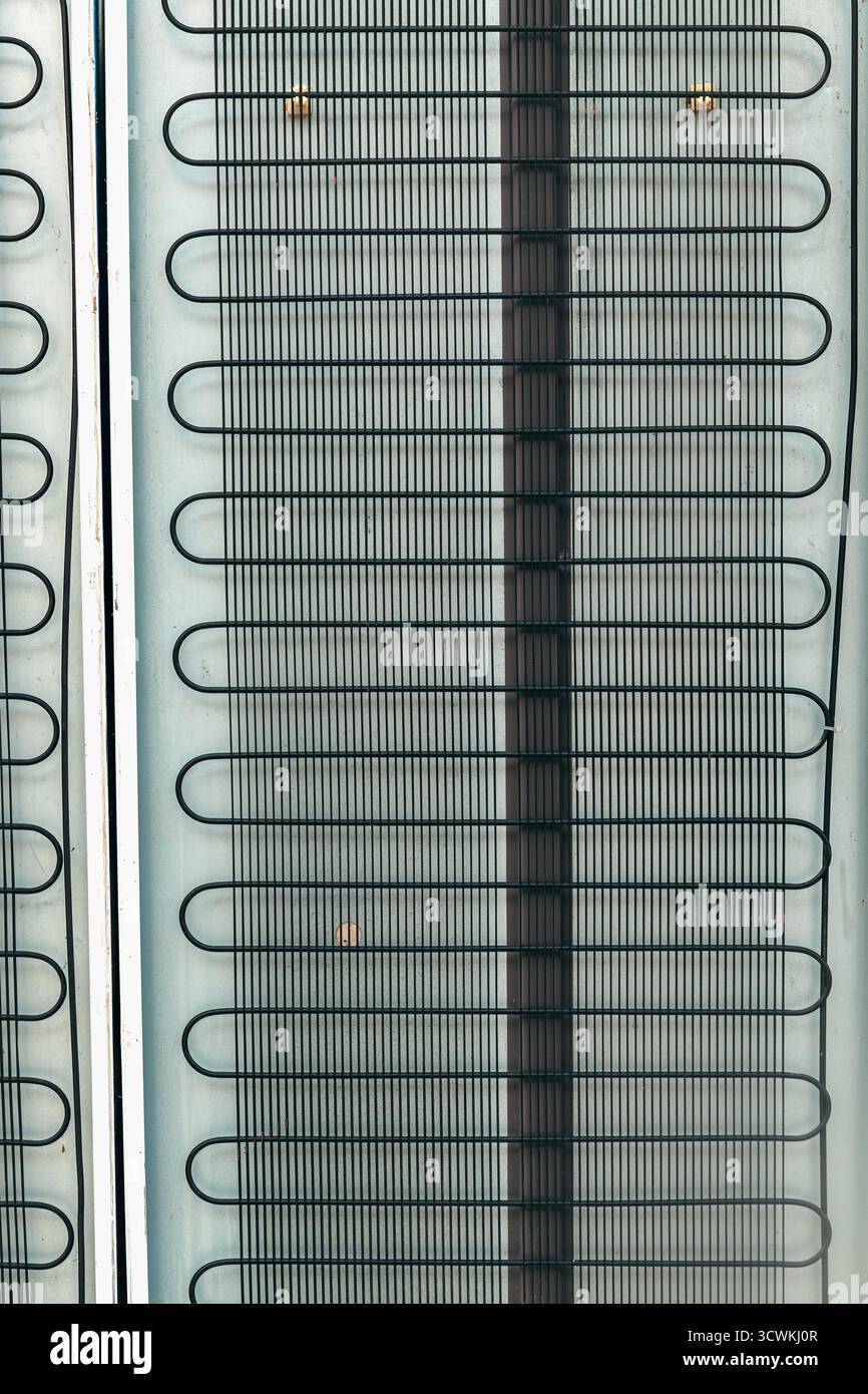 Nahaufnahme der Rückseite des Kühlschranks mit Kühlschlangen aus Metall, industrielles Detail in einfacher geometrischer Zusammensetzung. Vertikales Bild. Stockfoto