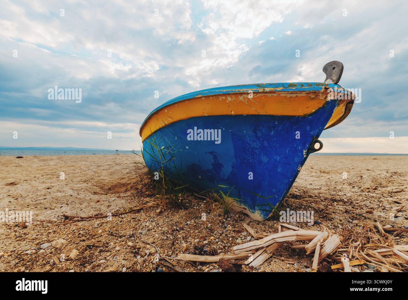 Altes Fischerboot ruht an einem Sandstrand unter einem dramatisch bewölkten Himmel. Die verwitterte Farbe und das rustikale Erscheinungsbild erinnern an Themen der Tradition, maritimen l Stockfoto