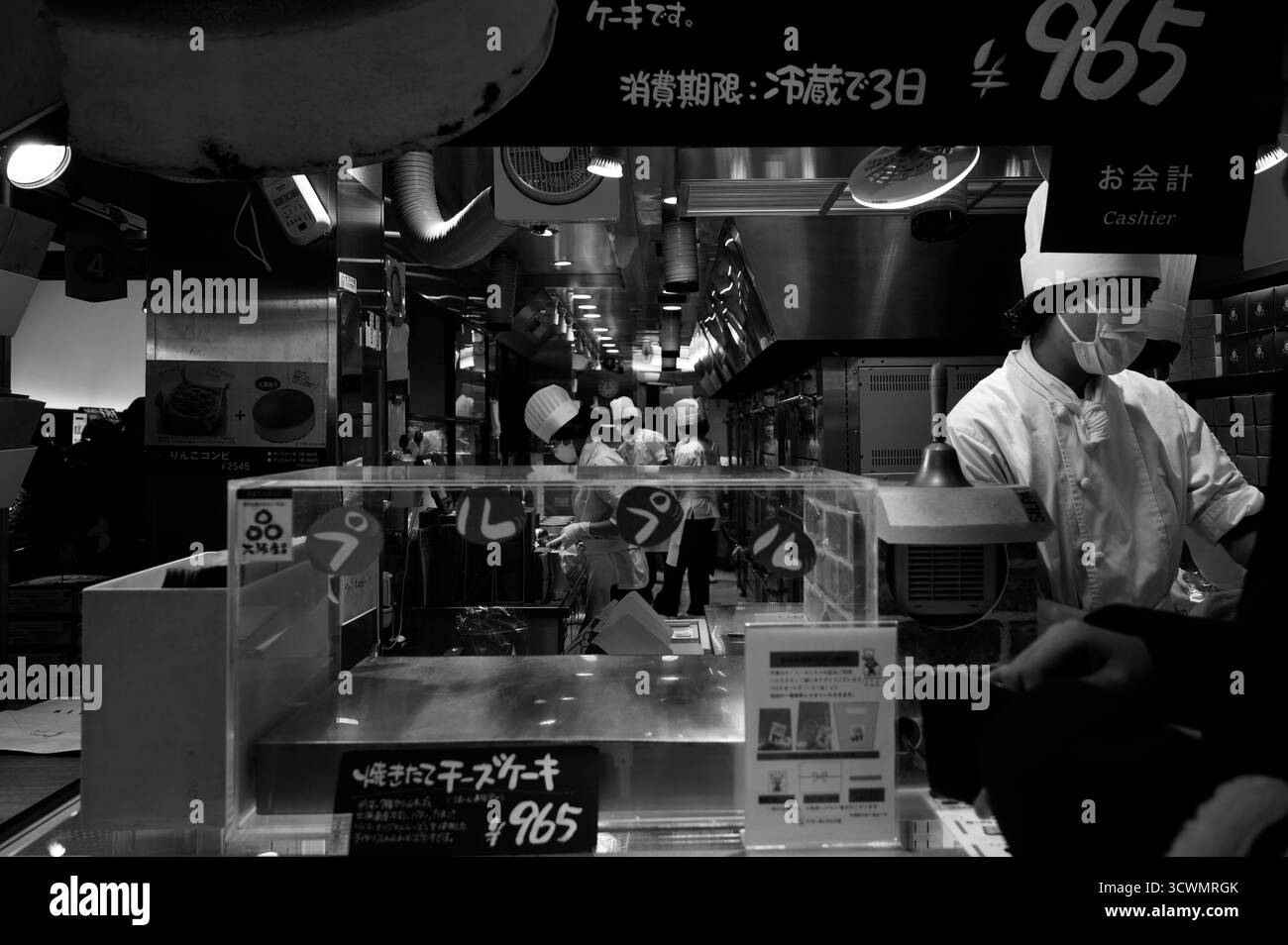 Die Köche bereiten den berühmten flauschigen japanischen Käsekuchen in einer geschäftigen Bäckerei in Schwarz-weiß zu Stockfoto