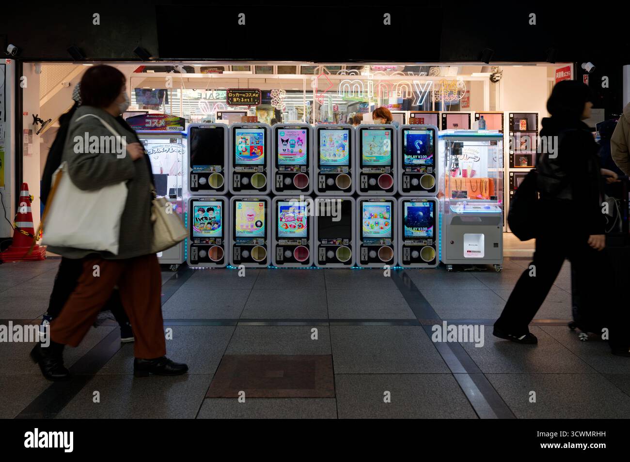 Fußgänger gehen an einer Reihe farbenfroher Gashapon- und Klauenmaschinen vorbei, die in einer Arkade von Osaka leuchten Stockfoto