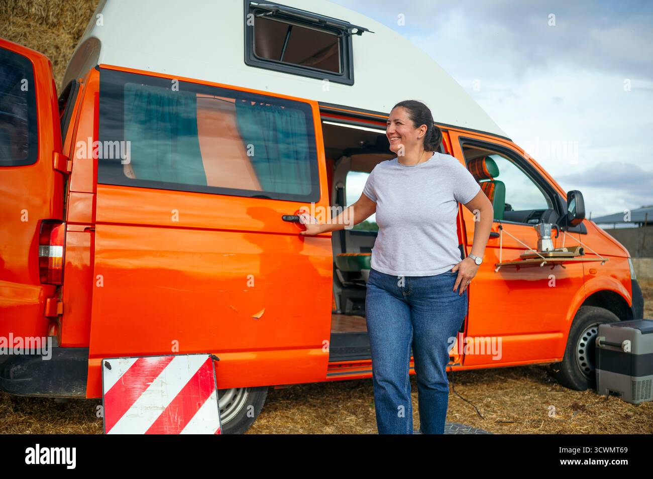 Frau, die neben einem orangen Wohnwagen steht und lächelt. Stockfoto