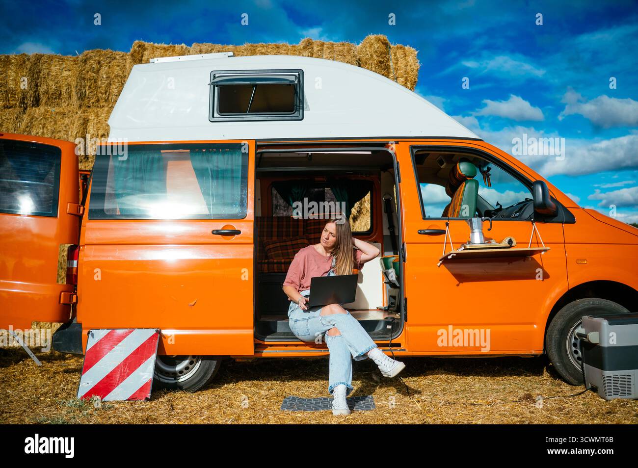 Frau, die am Laptop vor dem orangen Wohnmobil arbeitet. Stockfoto