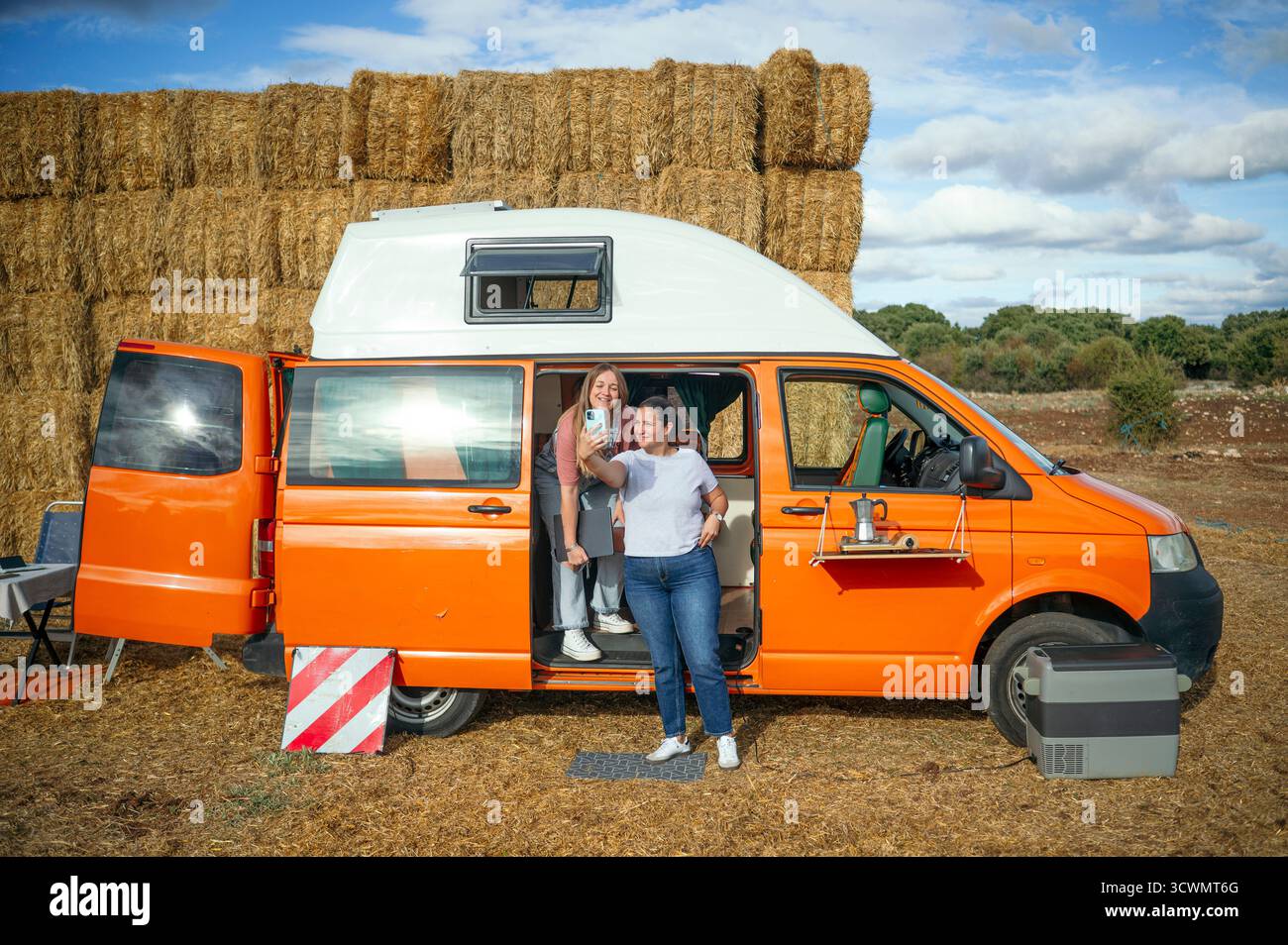 Zwei Frauen posieren für Selfie neben dem orangen Wohnmobil. Stockfoto
