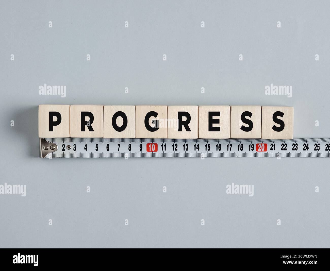 Holzwürfel, die Fortschritt schreiben, liegen über einem Maßband und repräsentieren das Konzept der Messung von Fortschritt und Wachstum Stockfoto