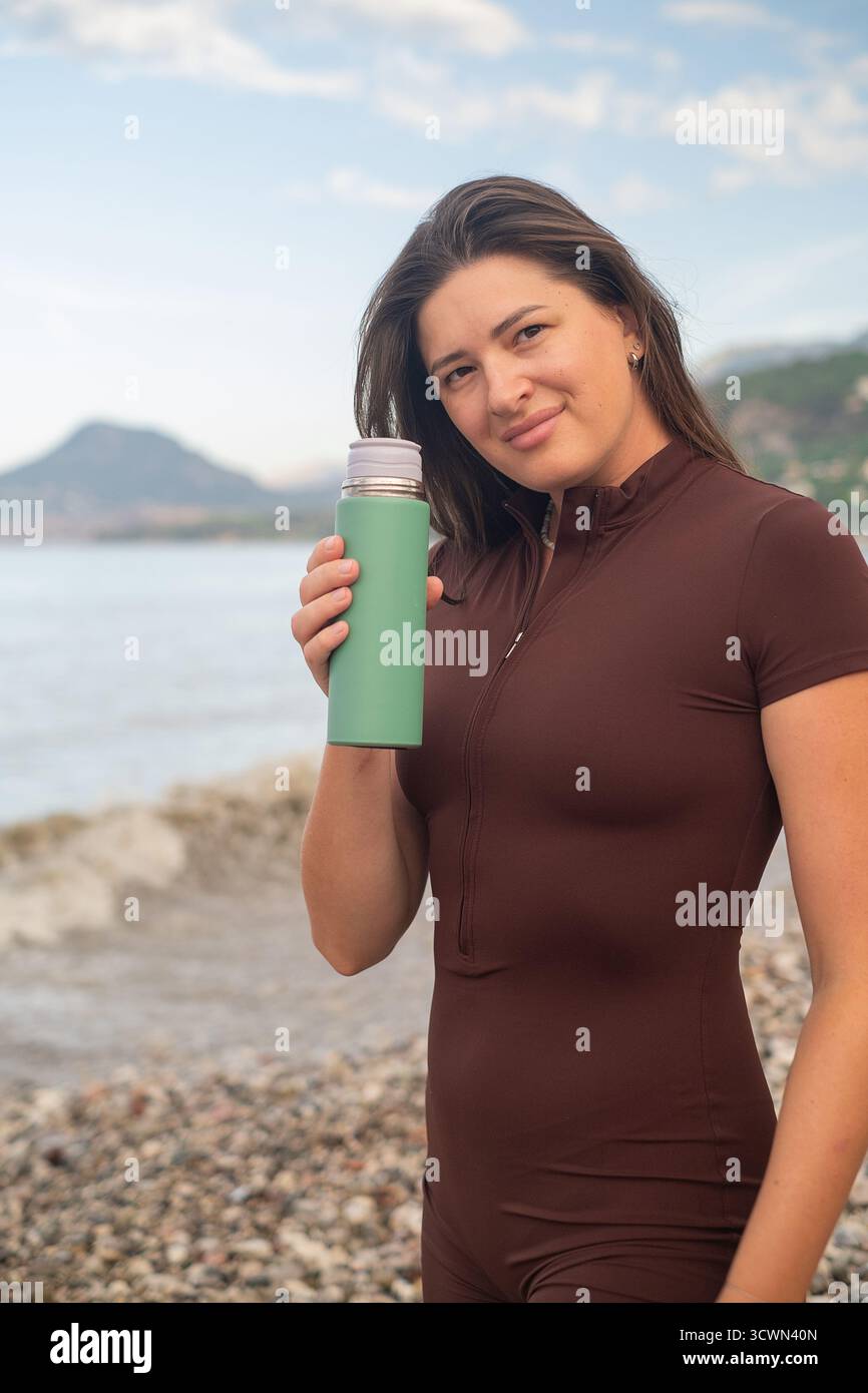 Frau genießt friedlichen Morgen am Meer, erfrischt Körper mit Wasser nach sportlicher Aktivität. Stockfoto