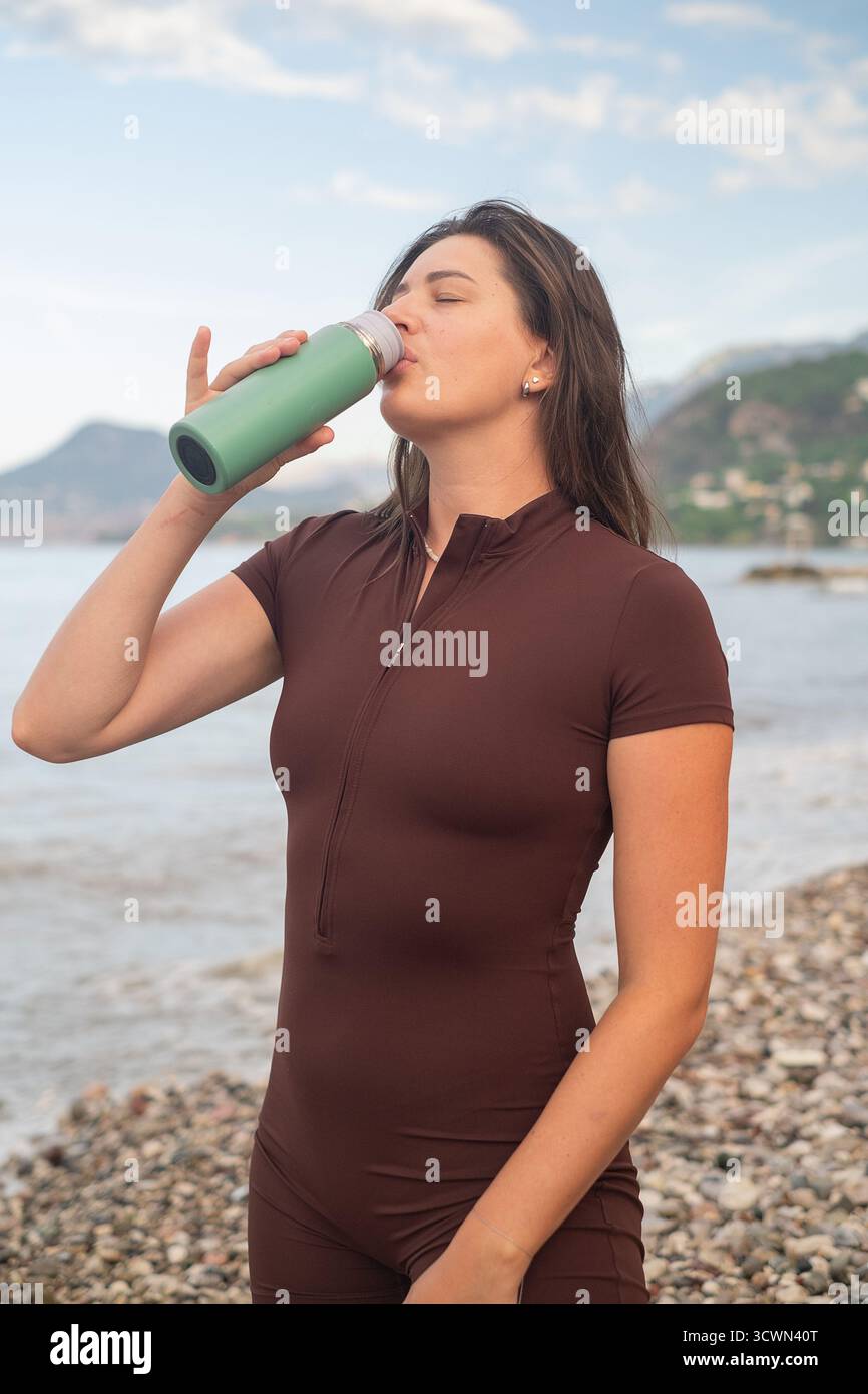 Frau in Sportbekleidung entspannend nach dem morgendlichen Workout am Meer Trinkwasser aus Flasche Outdoor Fitness Szene Stockfoto